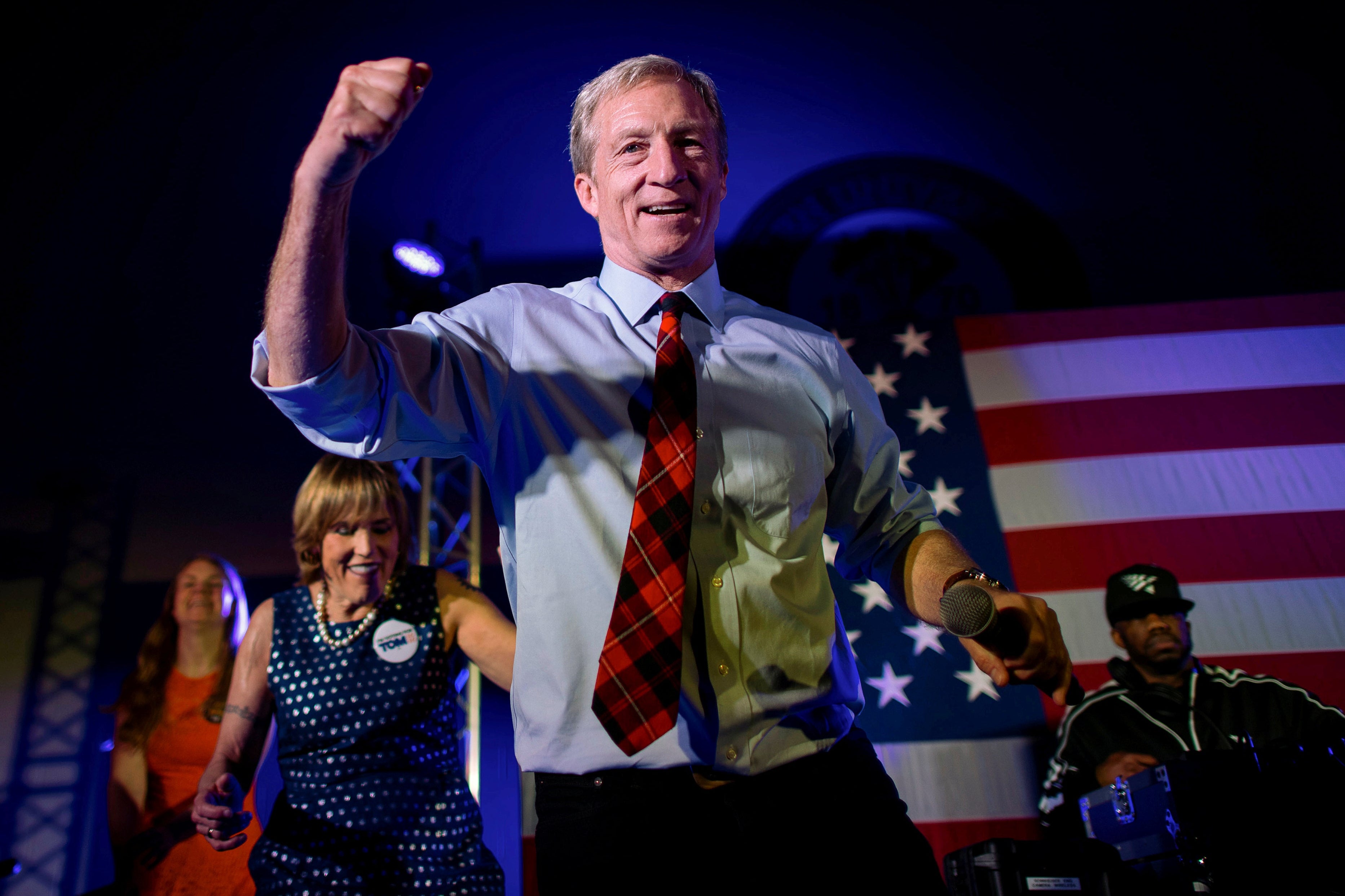 Tom Steyer dances onstage with rapper Juvenile on stage in front of an American flag. 