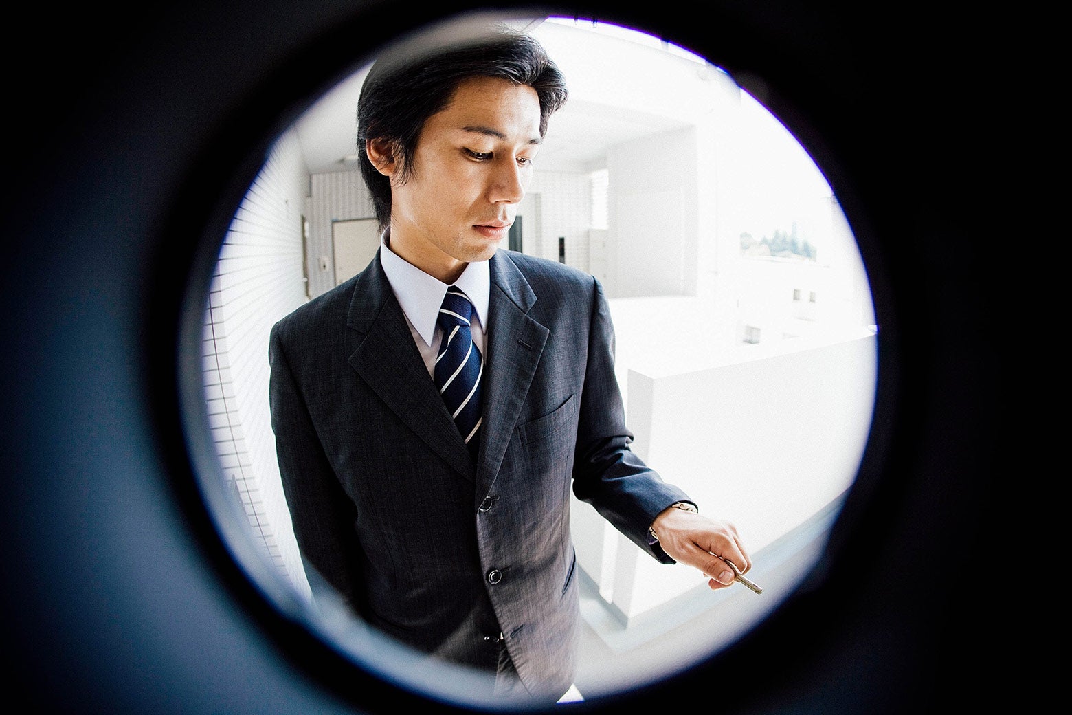 Fisheye peephole view of a man in a suit at the door.