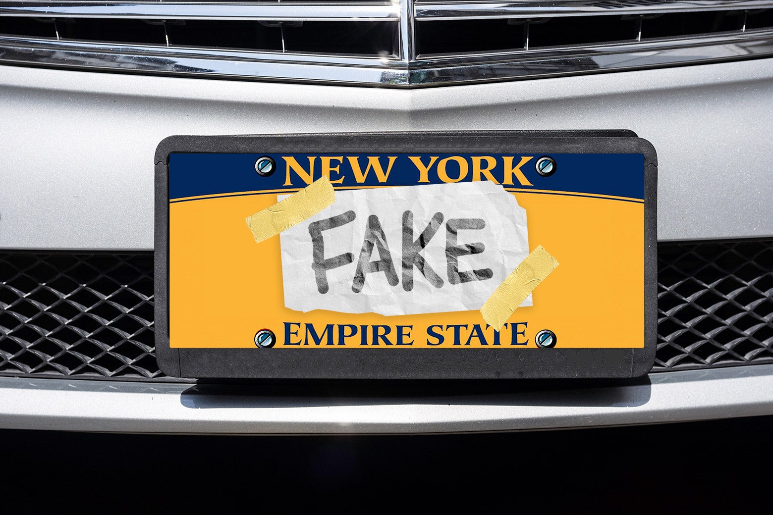 A car license plate with a piece of paper that says "FAKE" taped over it.