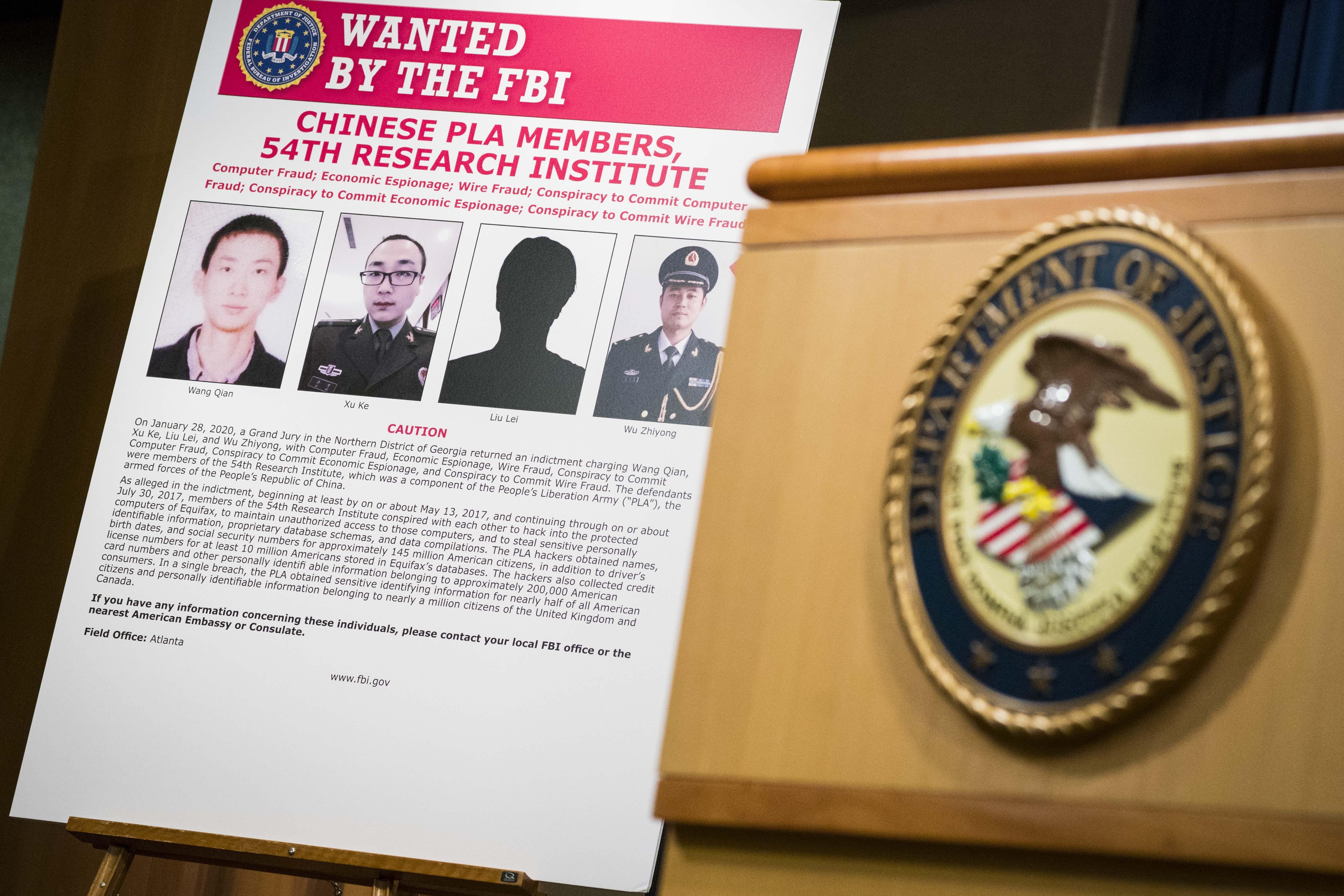 A sign that says "Wanted by the FBI" identifying four PLA members, next to a podium with the DOJ seal.