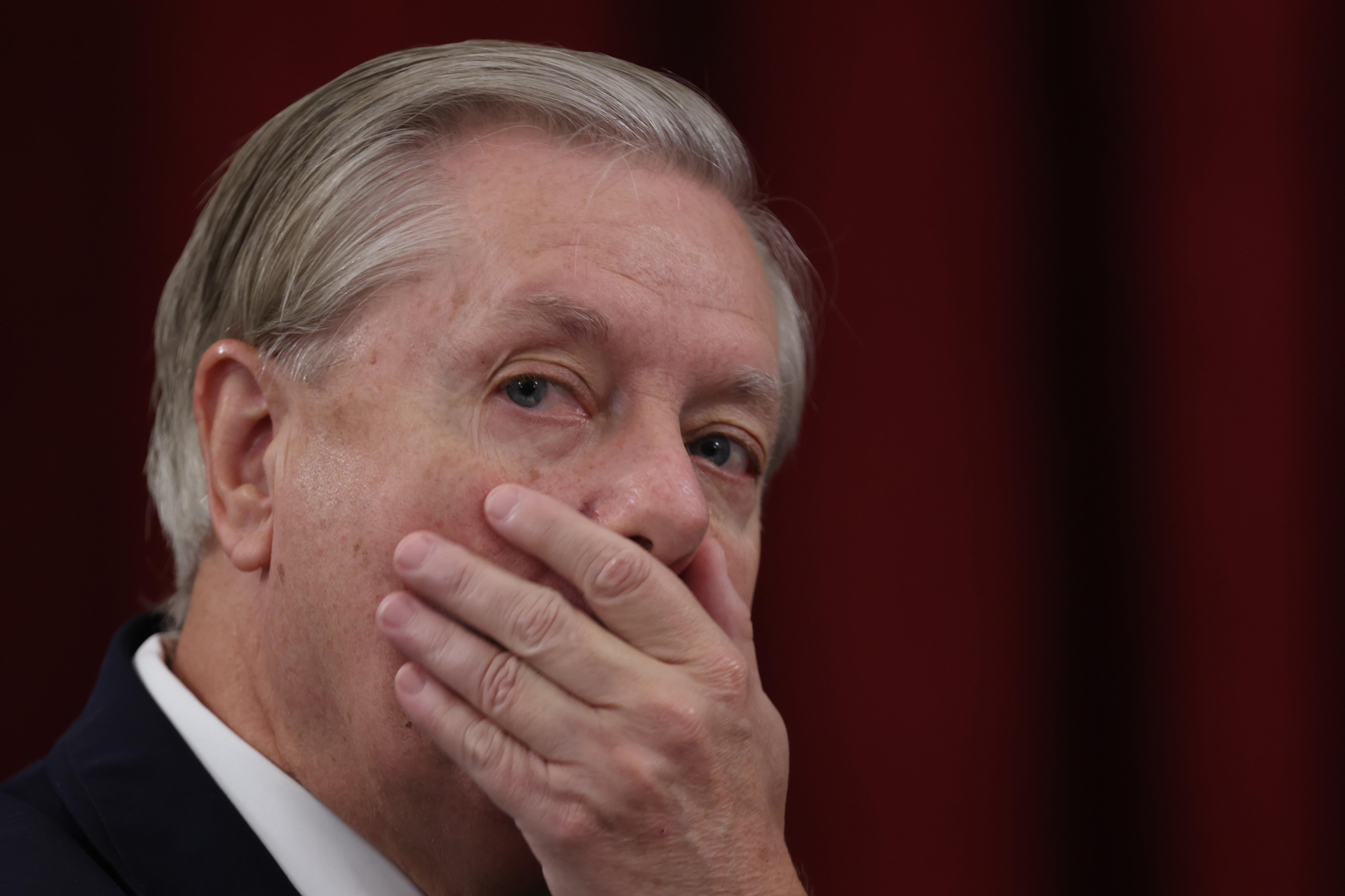 Lindsey Graham covers his mouth with his hand.