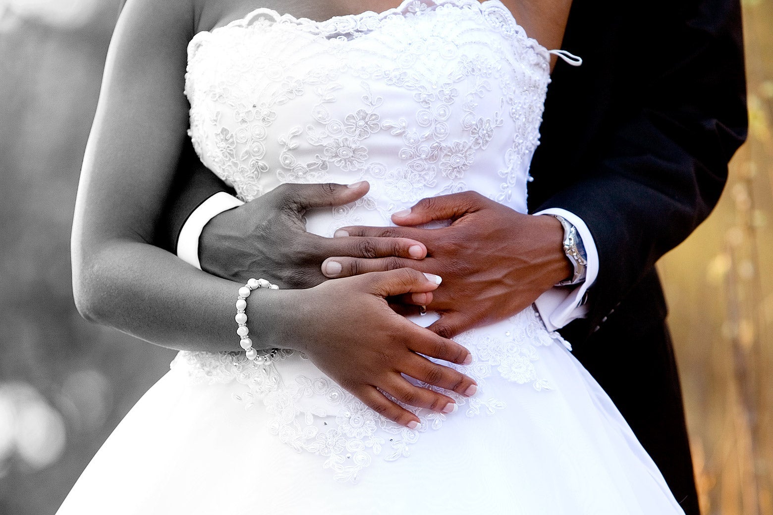 A bride and groom, with his arms wrapped around her waist. The left side of the image is greyscale, gradually transitioning to full color on the right.
