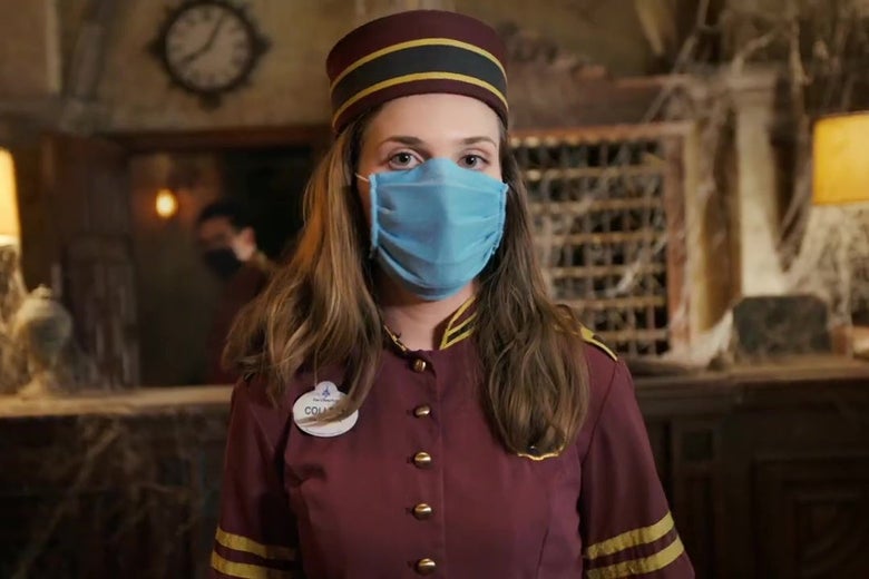 A Disney employee in a 1930s bellboy uniform and surgical mask stands in front of the cobweb-strewn front desk from Walt Disney World's Tower of Terror.