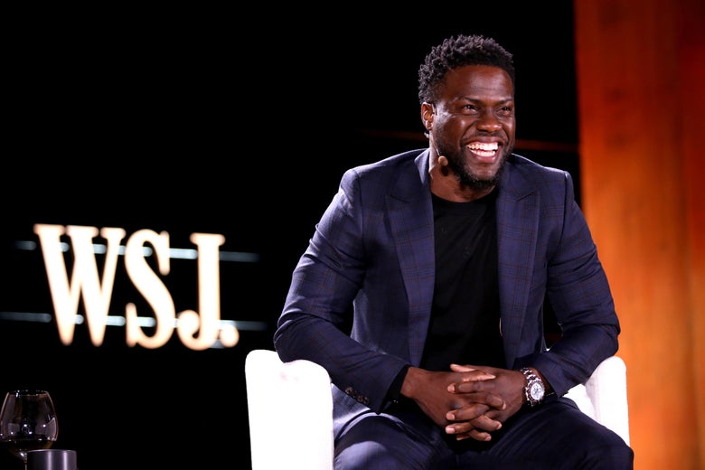 Kevin Hart sitting on a stage, smiling and laughing.