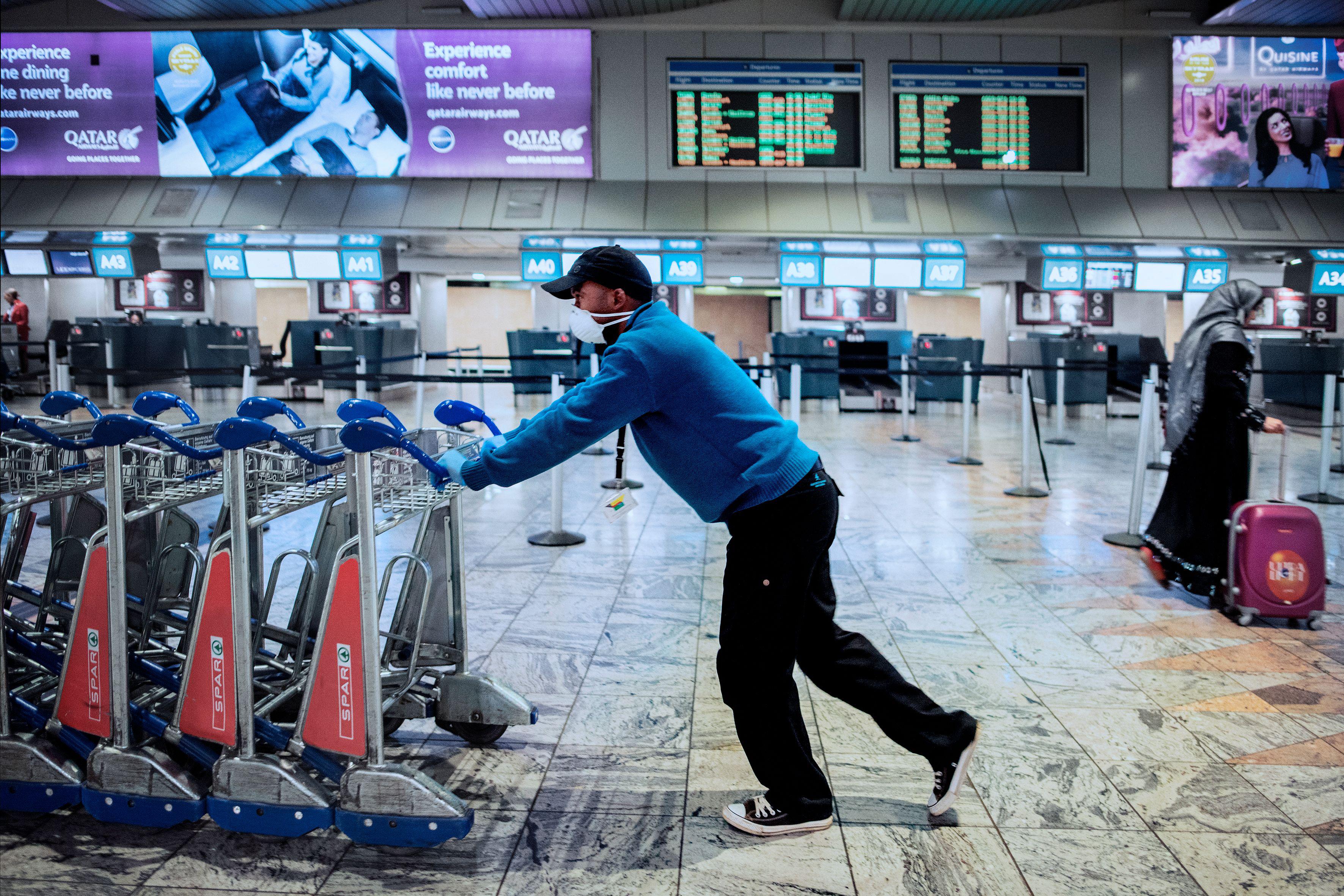 An Airports Company South Africa (ACSA) employee wears a face mask while pushing trolleys at the international departures terminal at the O.R. Tambo international airport in Johannesburg, on March 17, 2020. 