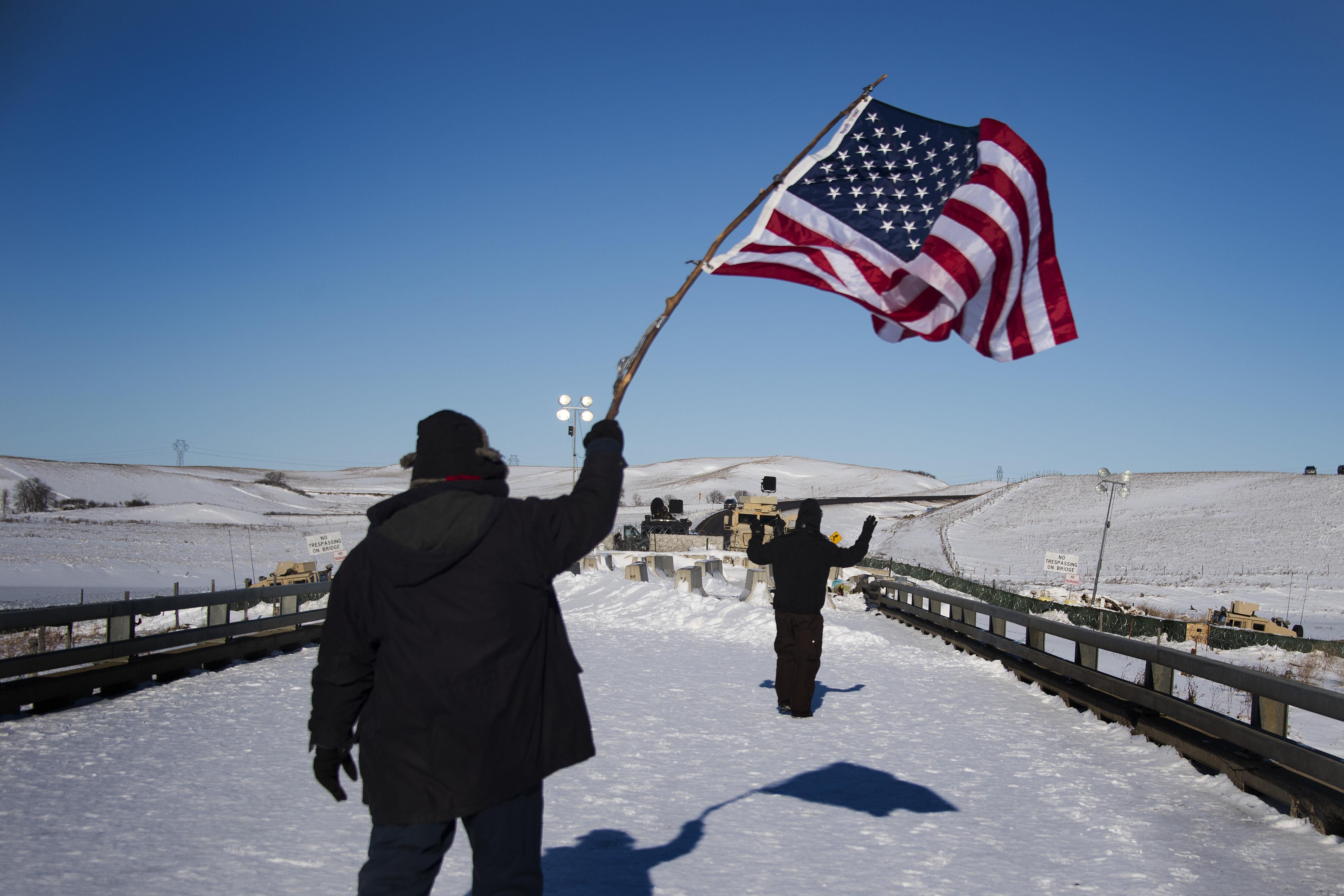 A man waves a U.S. flag as another man with arms raised walks toward a barricade.
