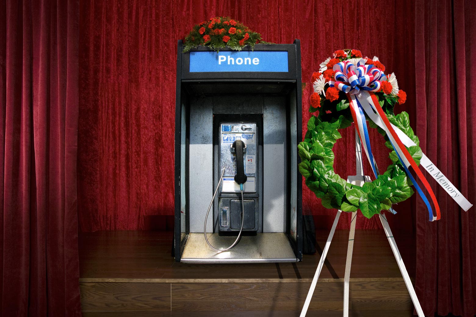 A payphone in front of a curtain, as in a funeral home, next to a funeral wreath.