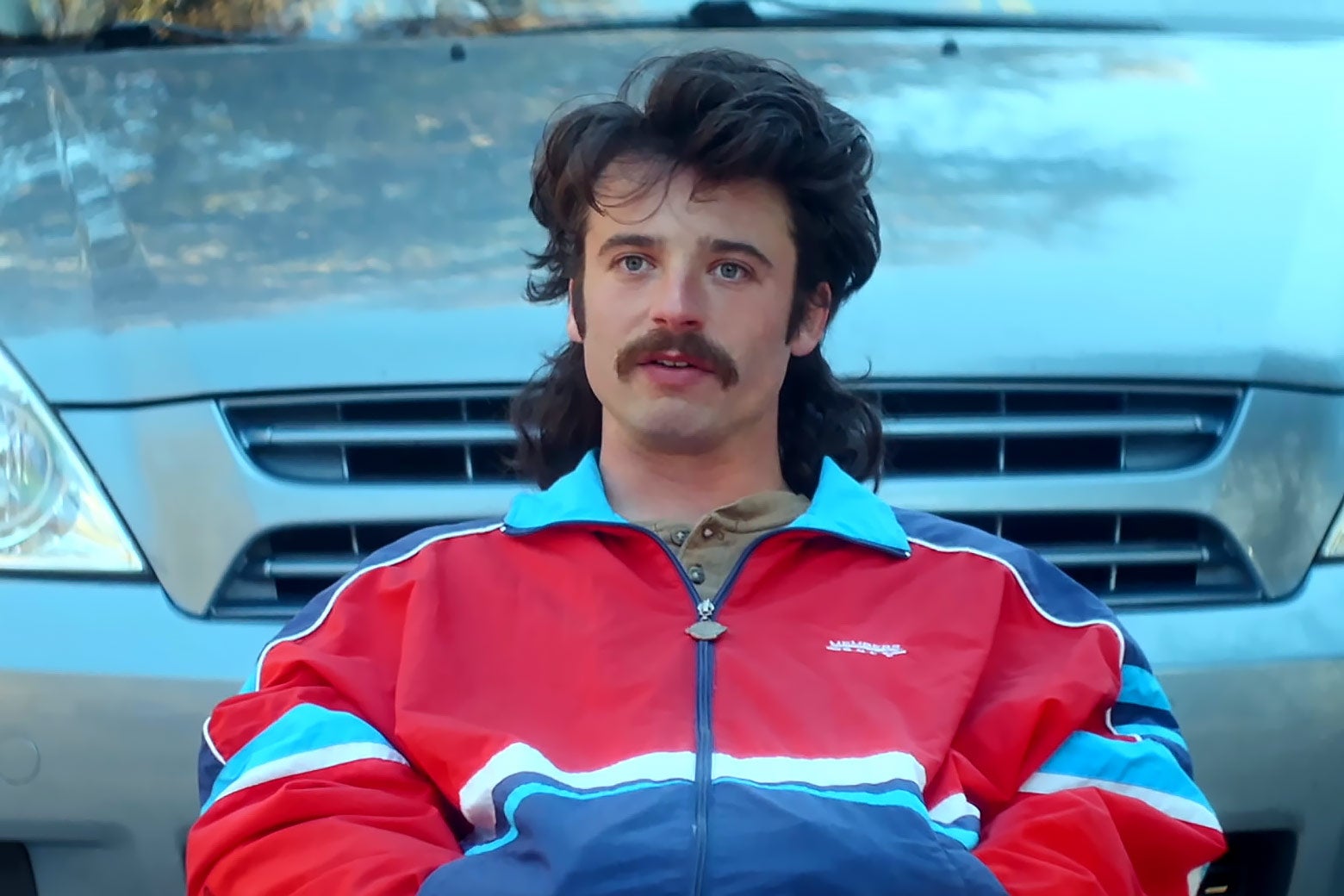 A white man looks incredulous and wears a mullet and a red-and-blue-striped shirt.