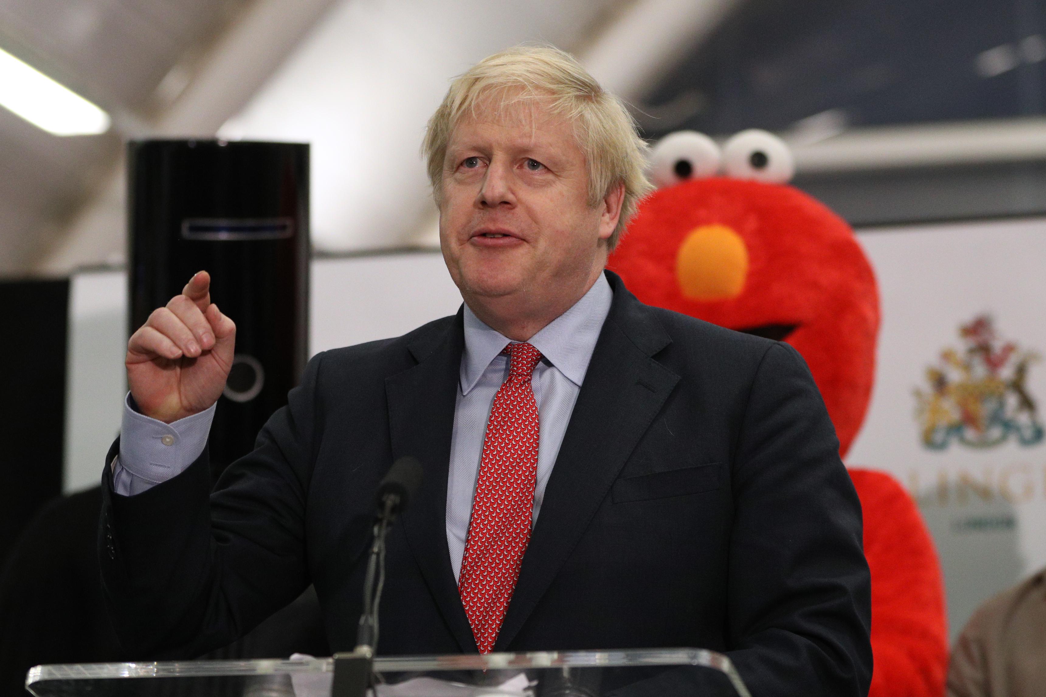 Boris Johnson gives a speech while a fellow candidate dressed as Sesame Street's Elmo stands behind him.