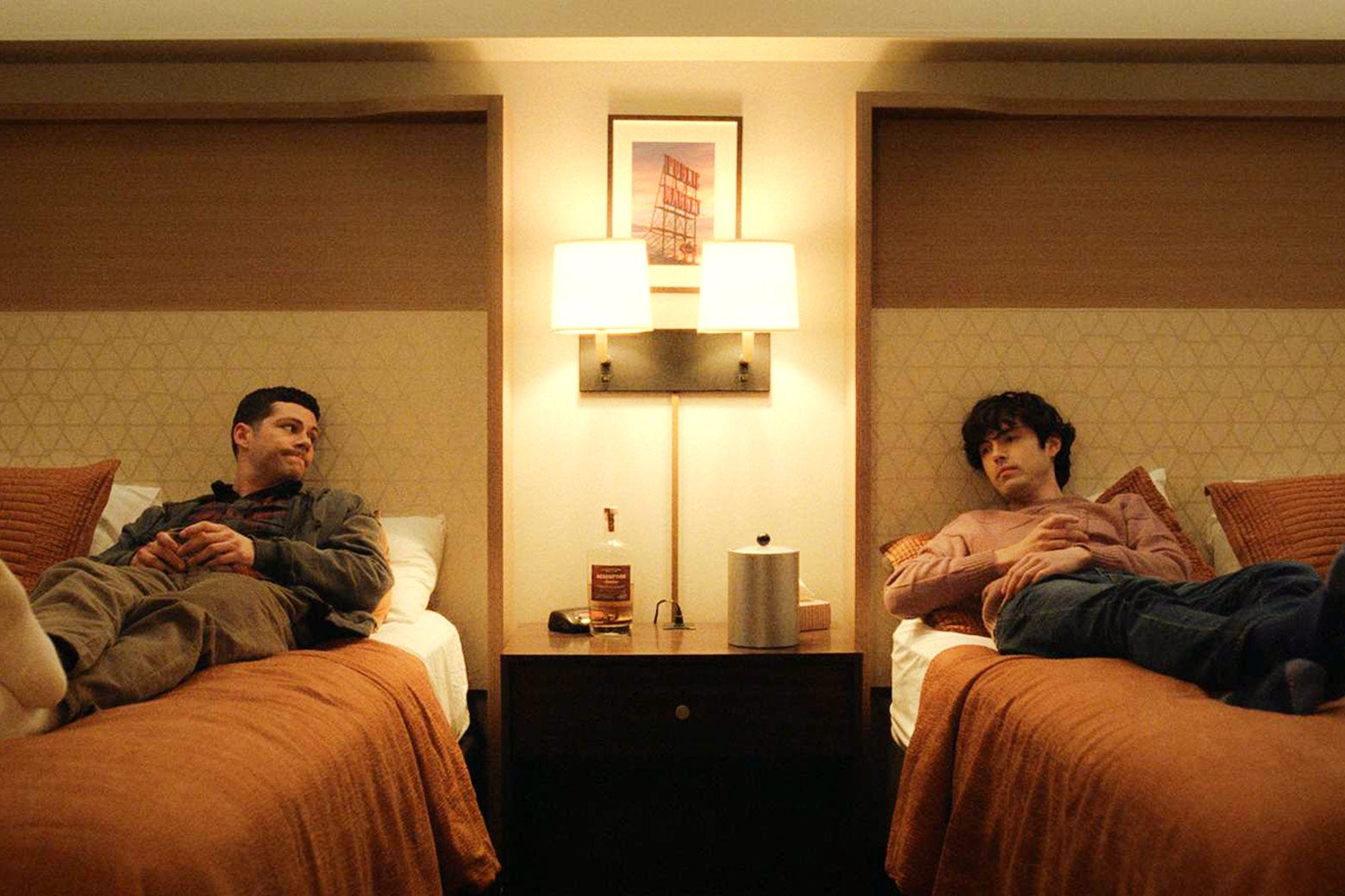 Dylan O'Brien's novel and James Sweeney's Dennis on twin beds opposite each other in a hotel room.