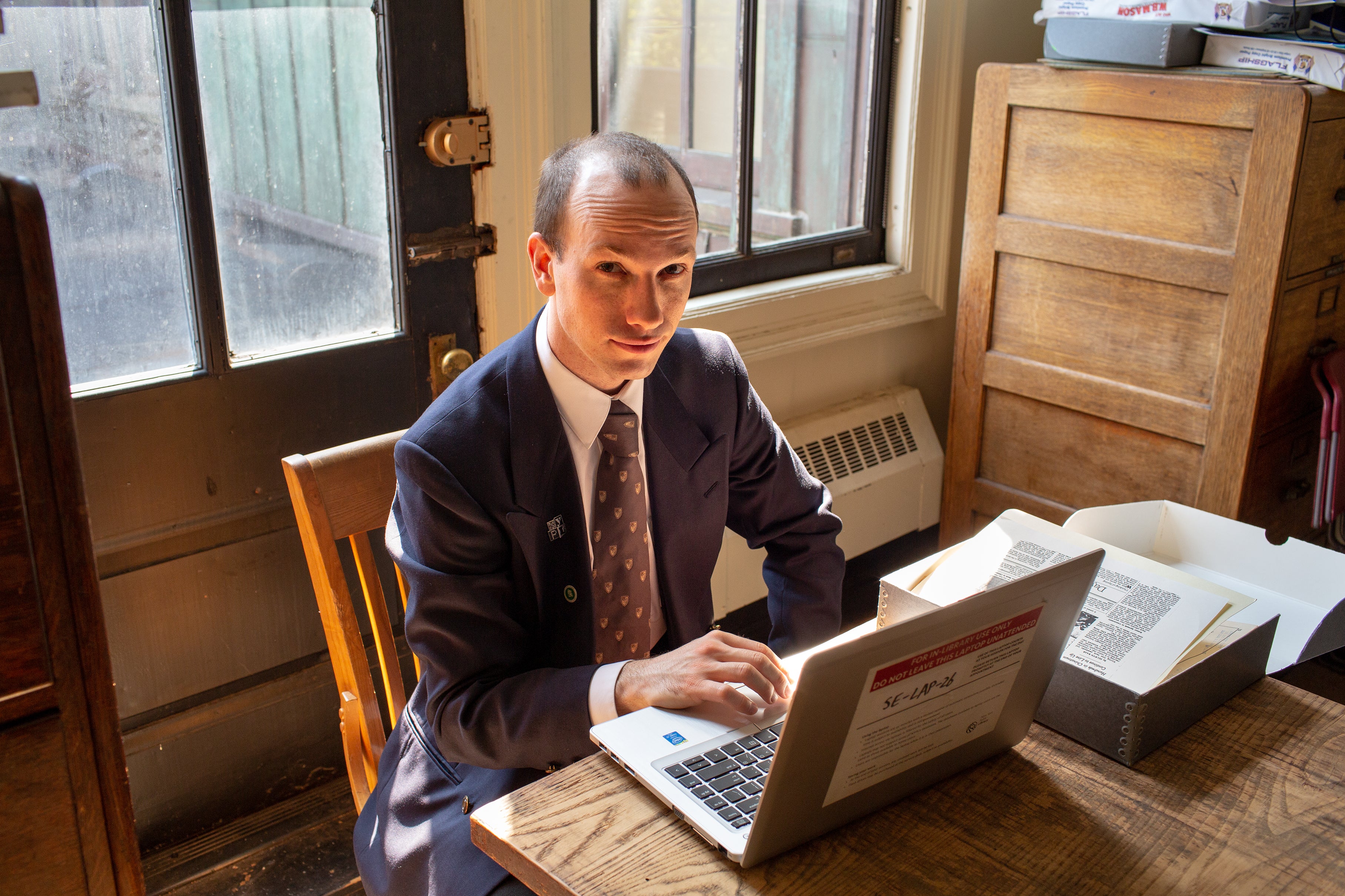 A man using a laptop, with a box of archival material open on the table.