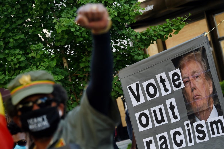 A demonstrator raises a fist in front of a sign that says "Vote Out Racism" with a picture of President Donald Trump.