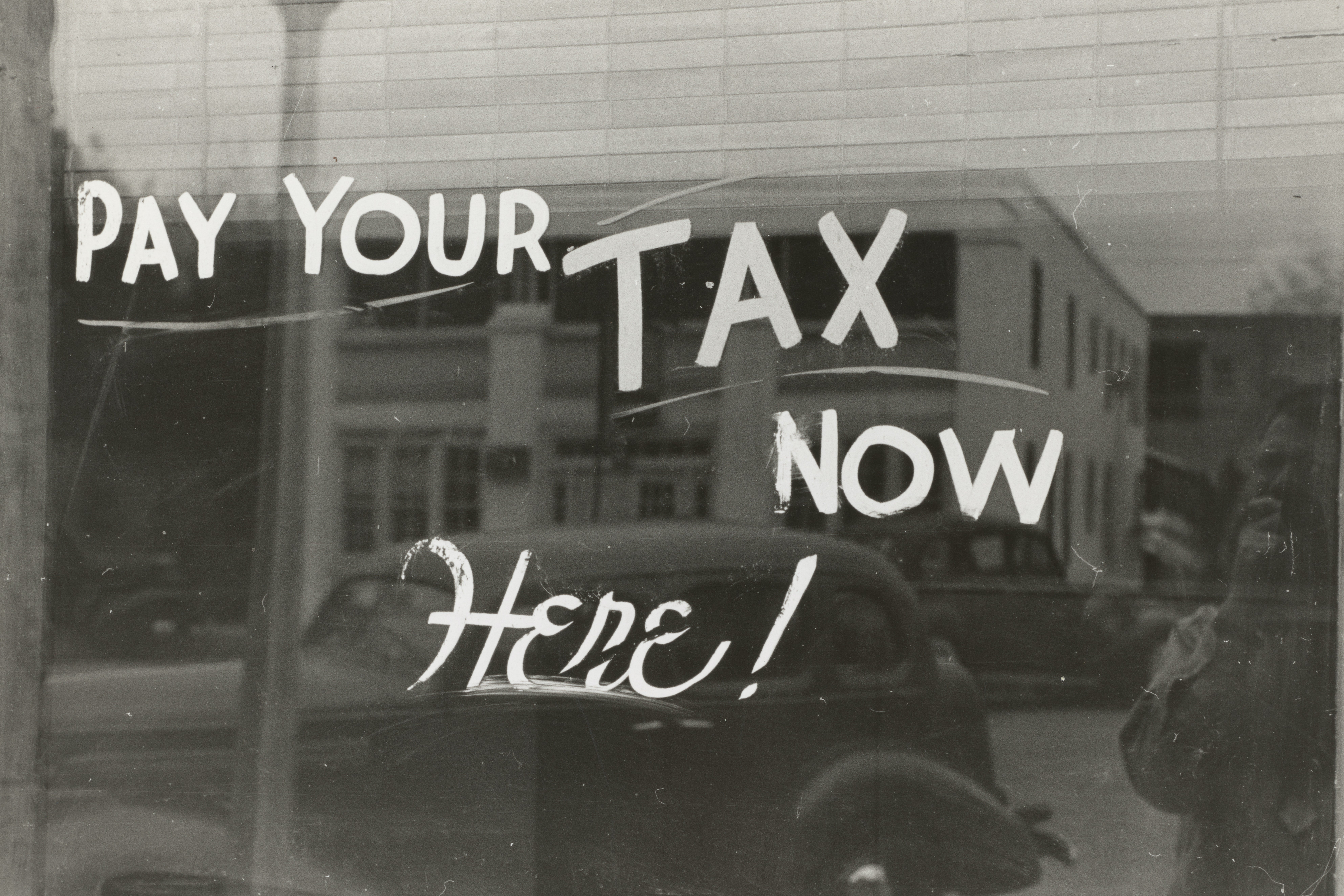 The words "Pay your tax now here!" written on a window that also reflects an old-timey car.