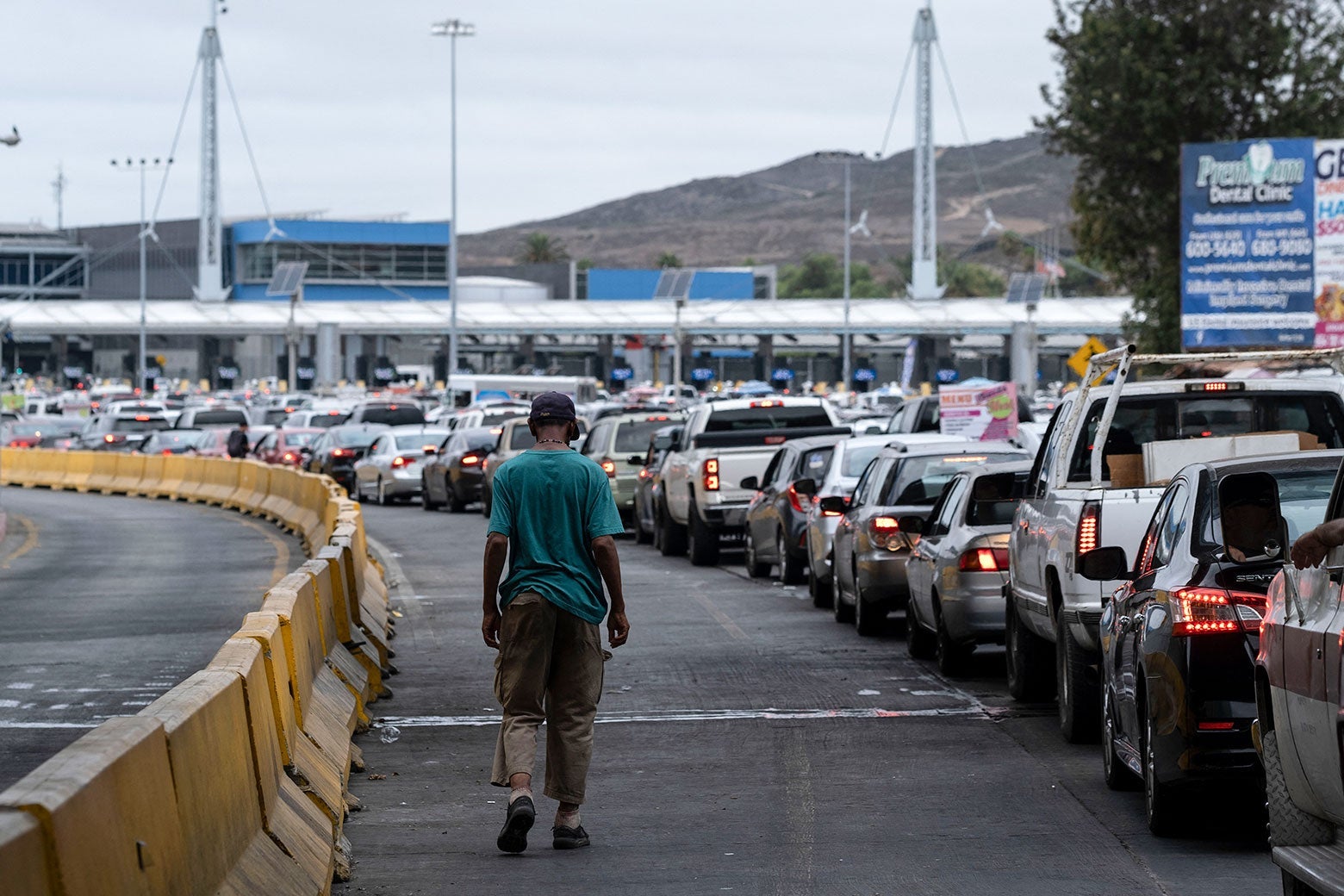A man walks alone beside a line of cars stopped at the border crossing.
