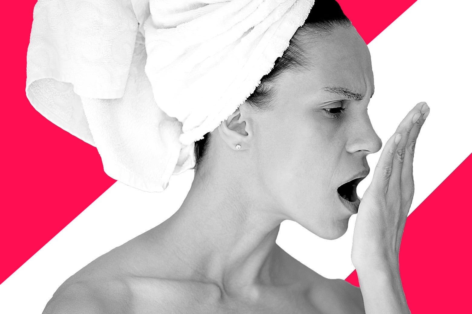 A woman w/ a towel on her head trying to smell her own breath against her palm.