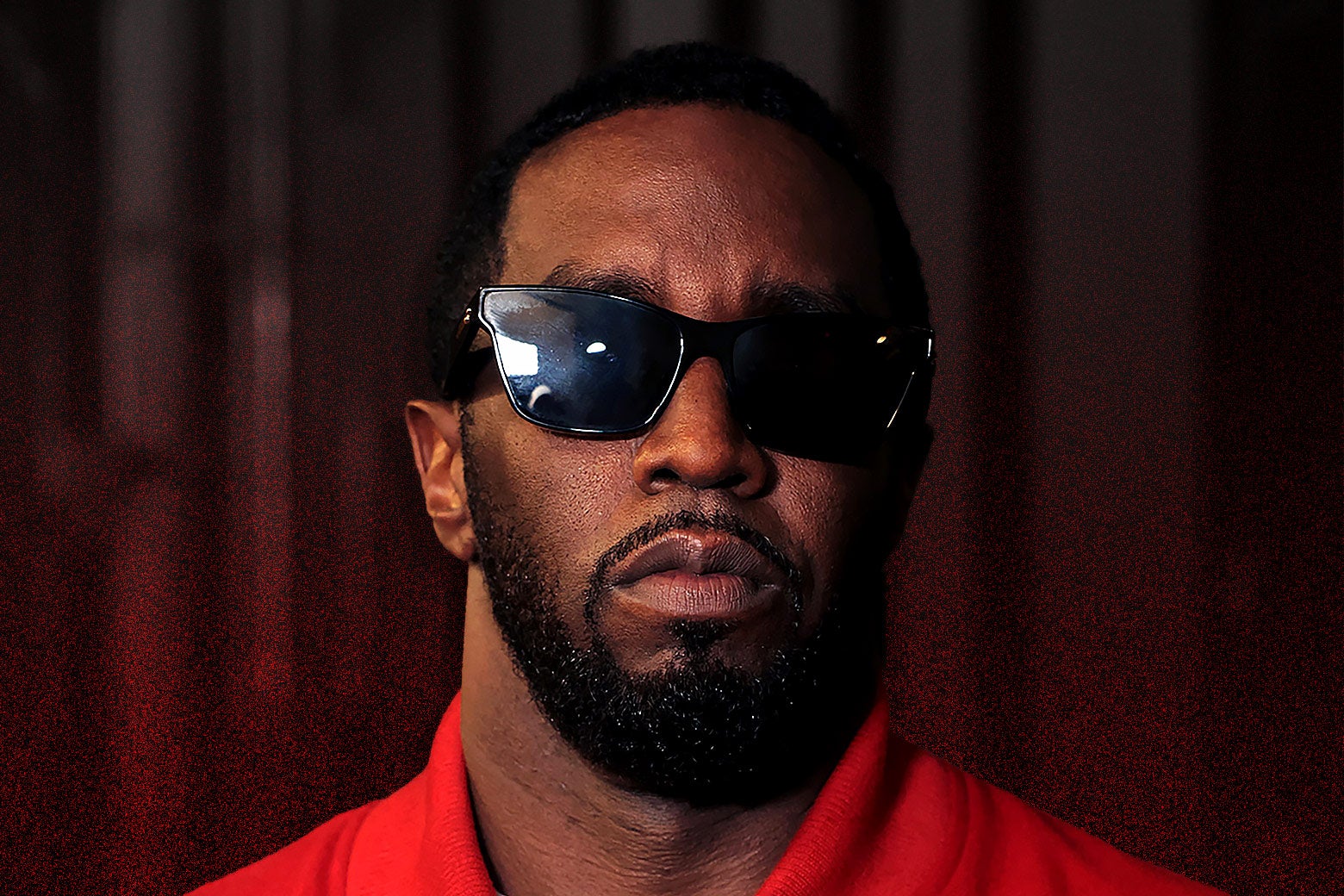 Sean "Diddy" Combs, expressionless, wears a red jacket and dark sunglasses.