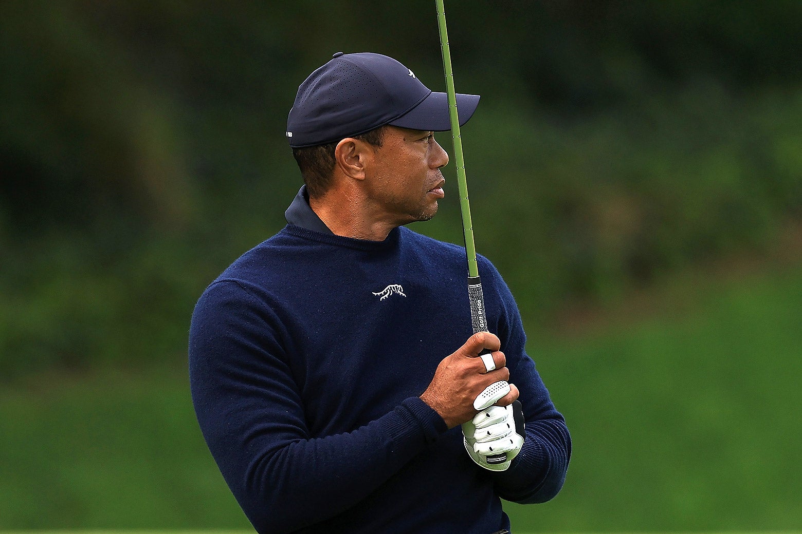Tiger Woods holds his club upright in front of him and gazes down the hole.