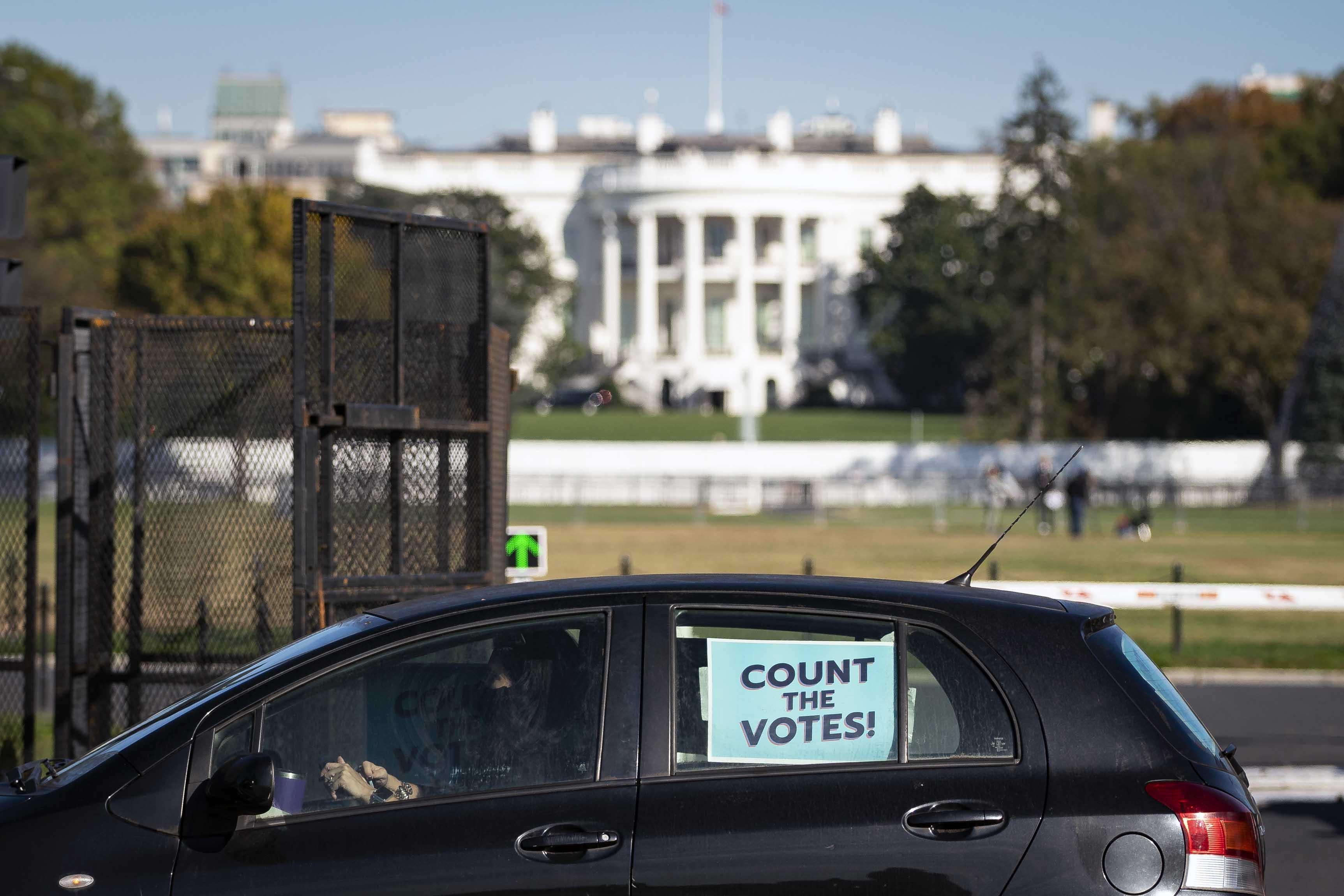 A van with a sign "Count the Votes" posted on the window is parked outside of the White House gate.