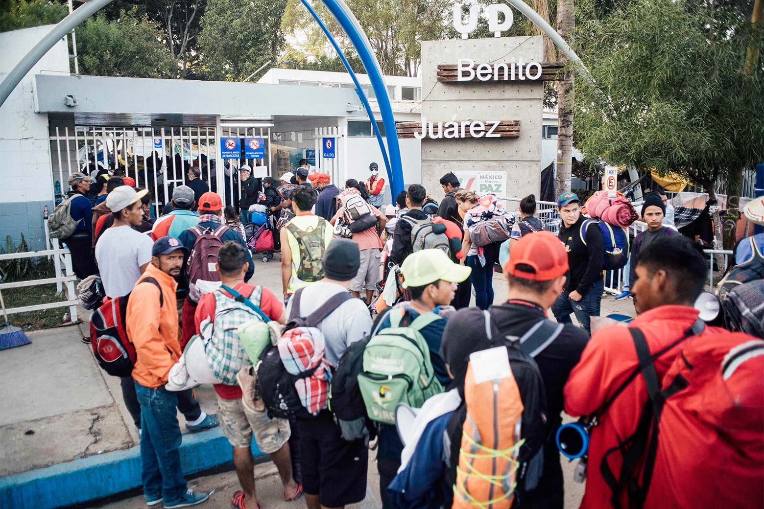 A crowd of people wearing backpacks standing outside of a stadium gate.