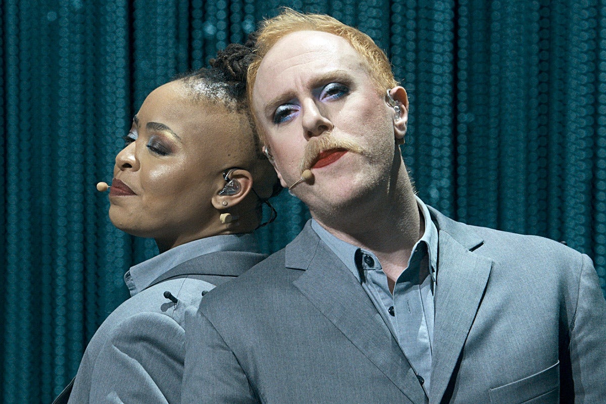 The two dancers lean their heads back against each other. They are both wearing matching gray suits.