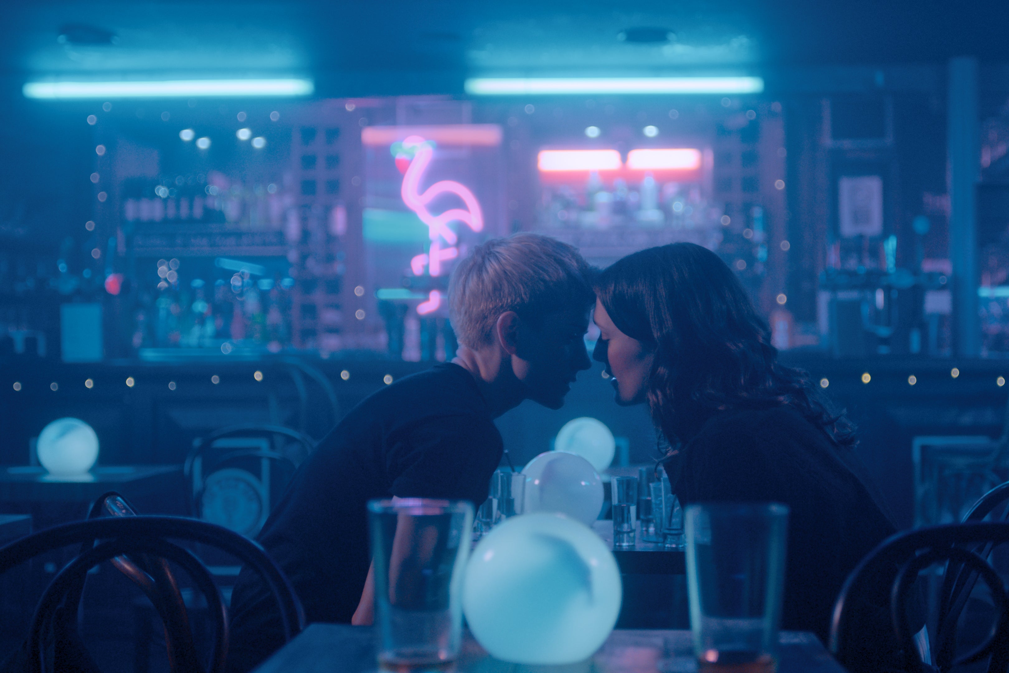 Two women lean in to kiss in a dark bar
