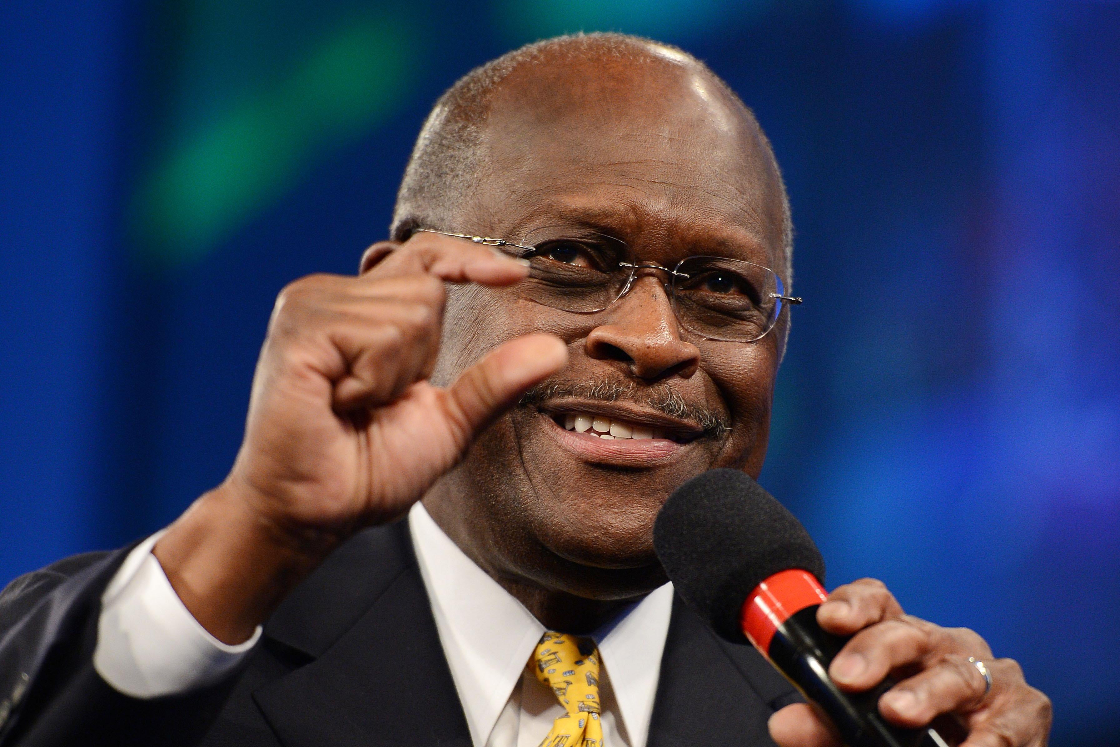 Herman Cain holds a microphone and gestures with his other hand.