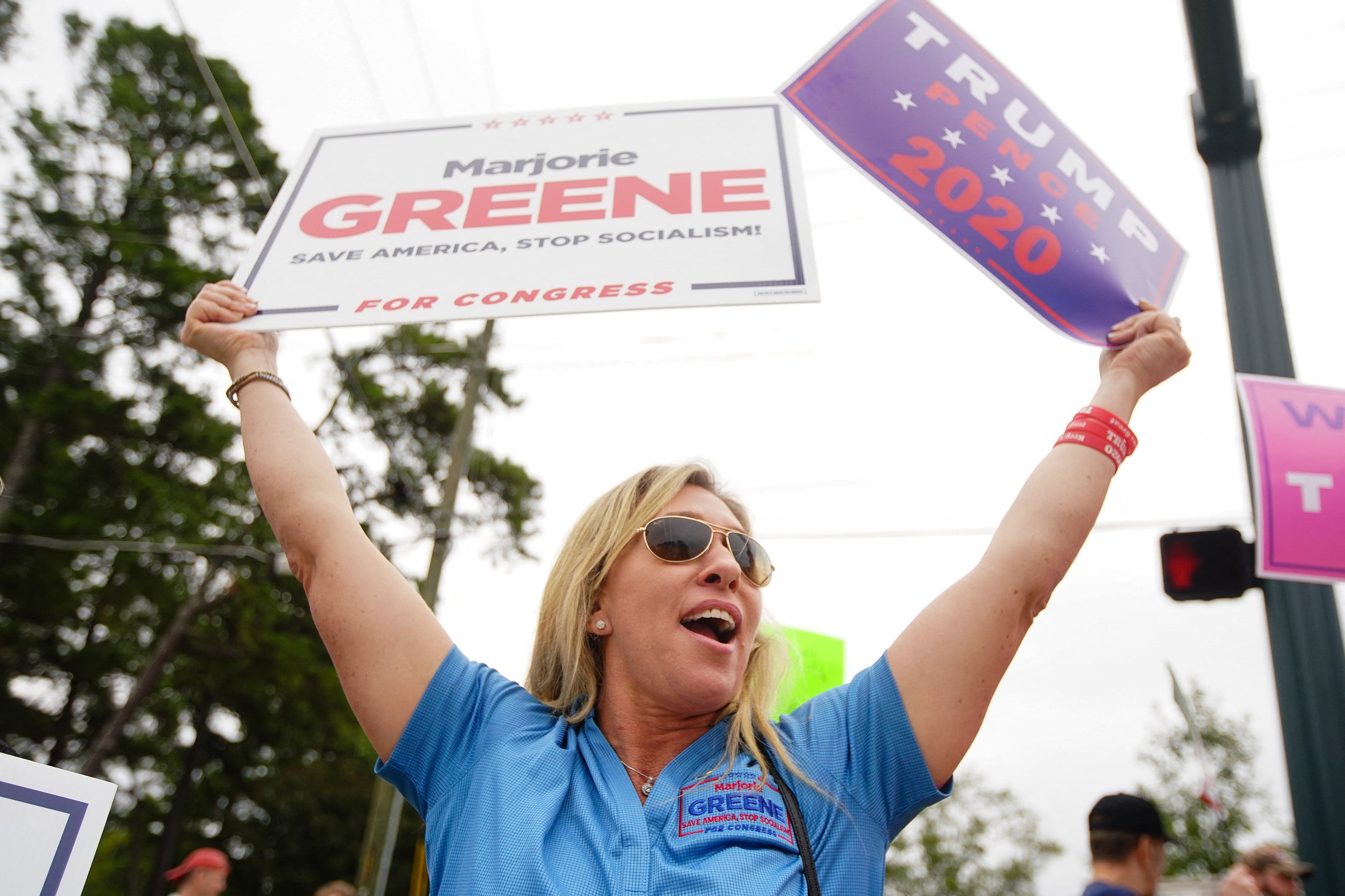 Greene holds up campaign signs in support of her and Donald Trump.
