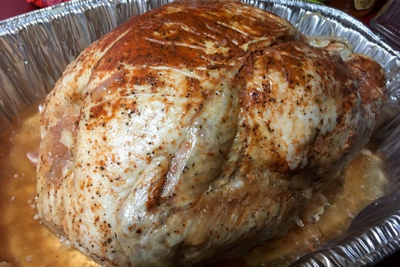 A turkey covered in red-ish seasoning in a foil roasting pan.