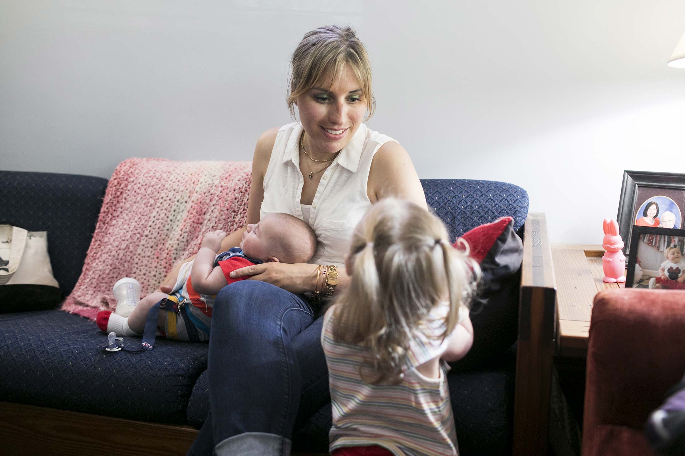 Celeste Blau sits on the couch holding her son Finneas while playing with Clementine.