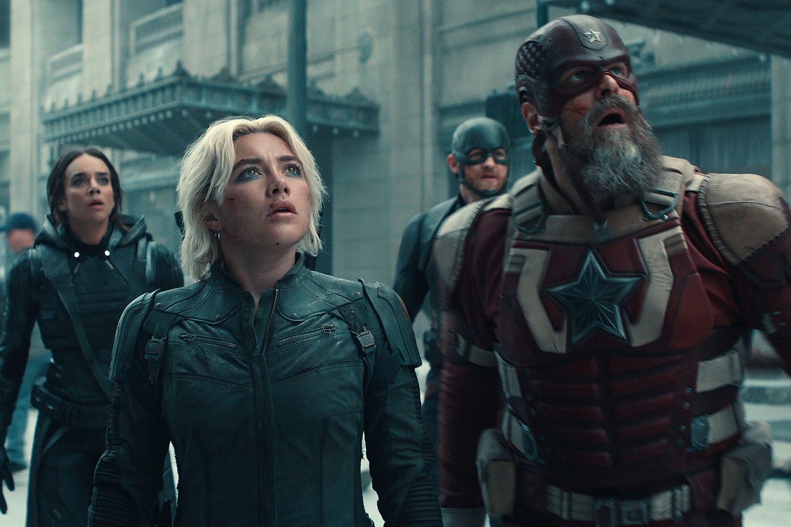 A group of Avengers look up in shock, standing on a dusty, debris-covered street.