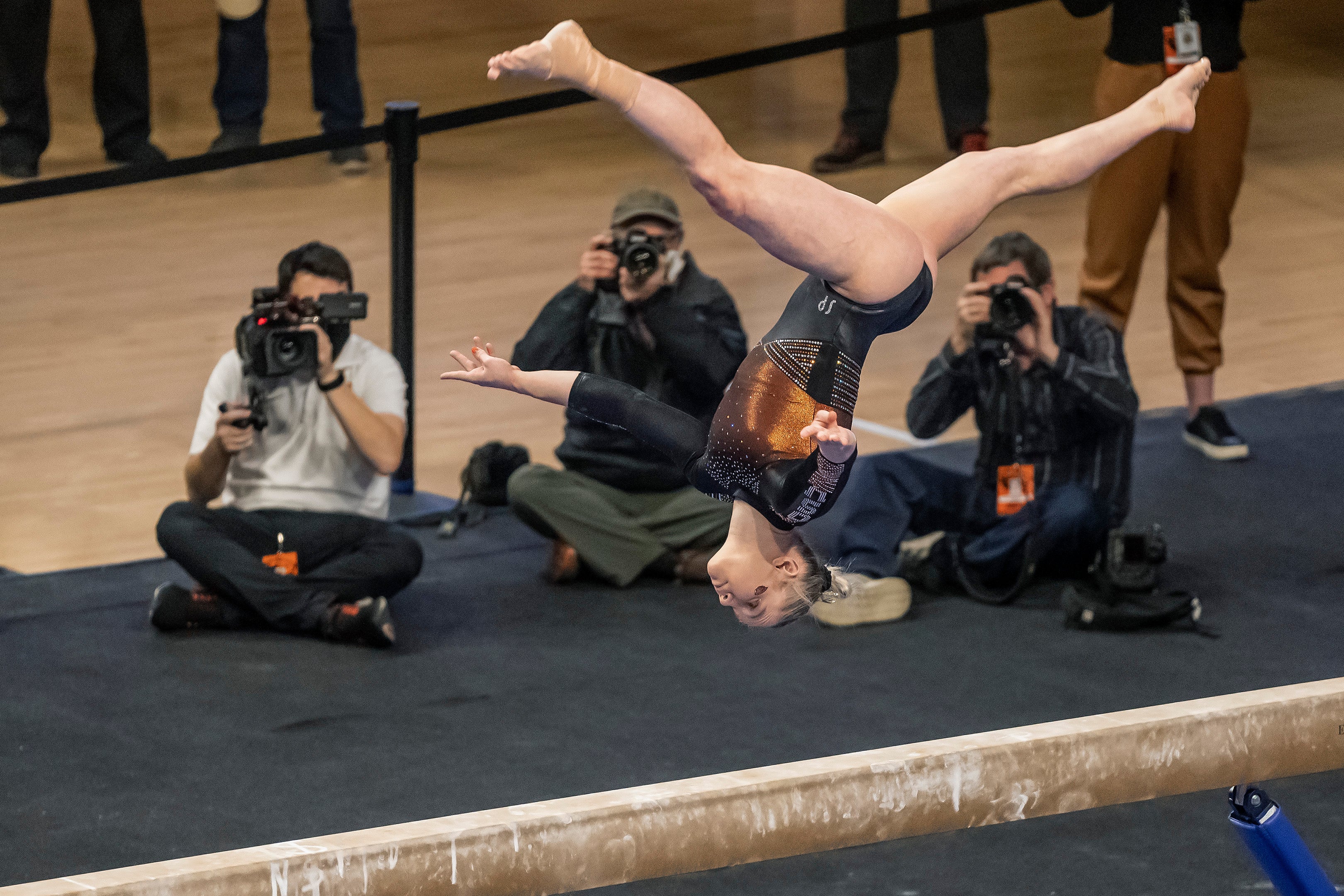 Jade Carey flipping upside down above the balance beam with cameramen filming her in the background.