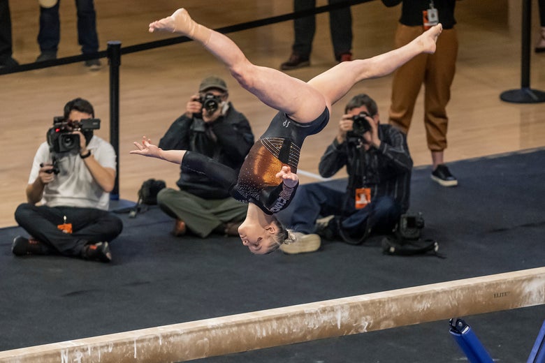Jade Carey flipping upside down above the balance beam with cameramen filming her in the background.