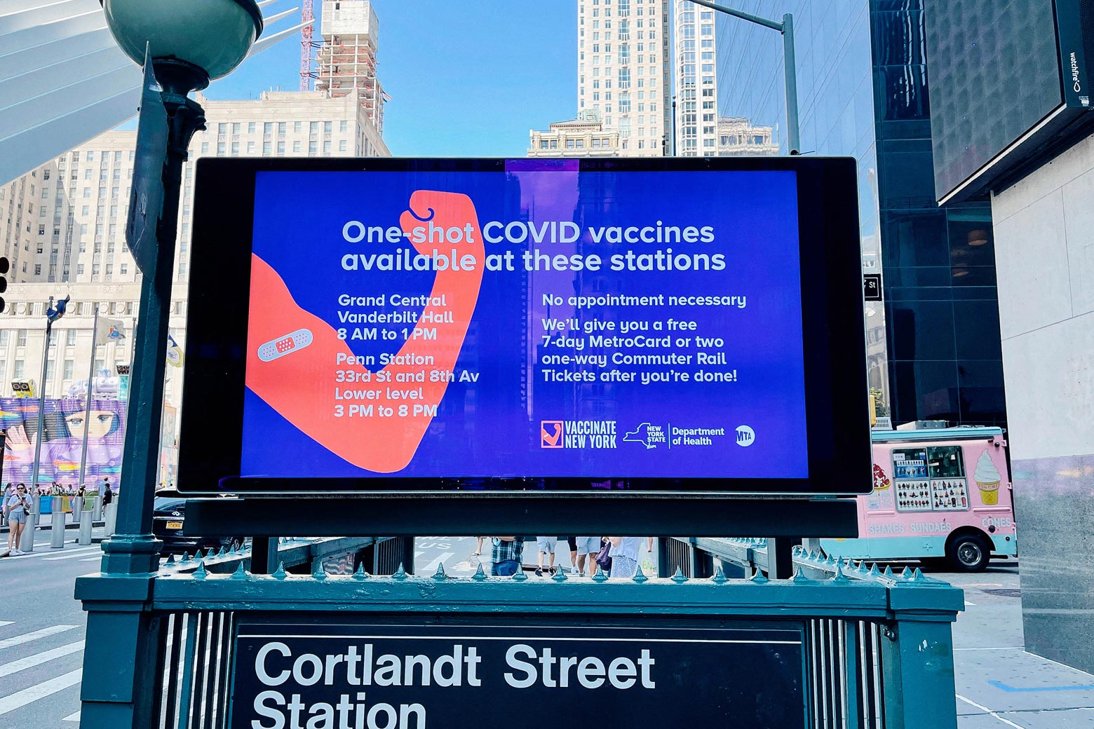 A screen advertising transit rewards for COVID-19 vaccination above the entrance to a subway station