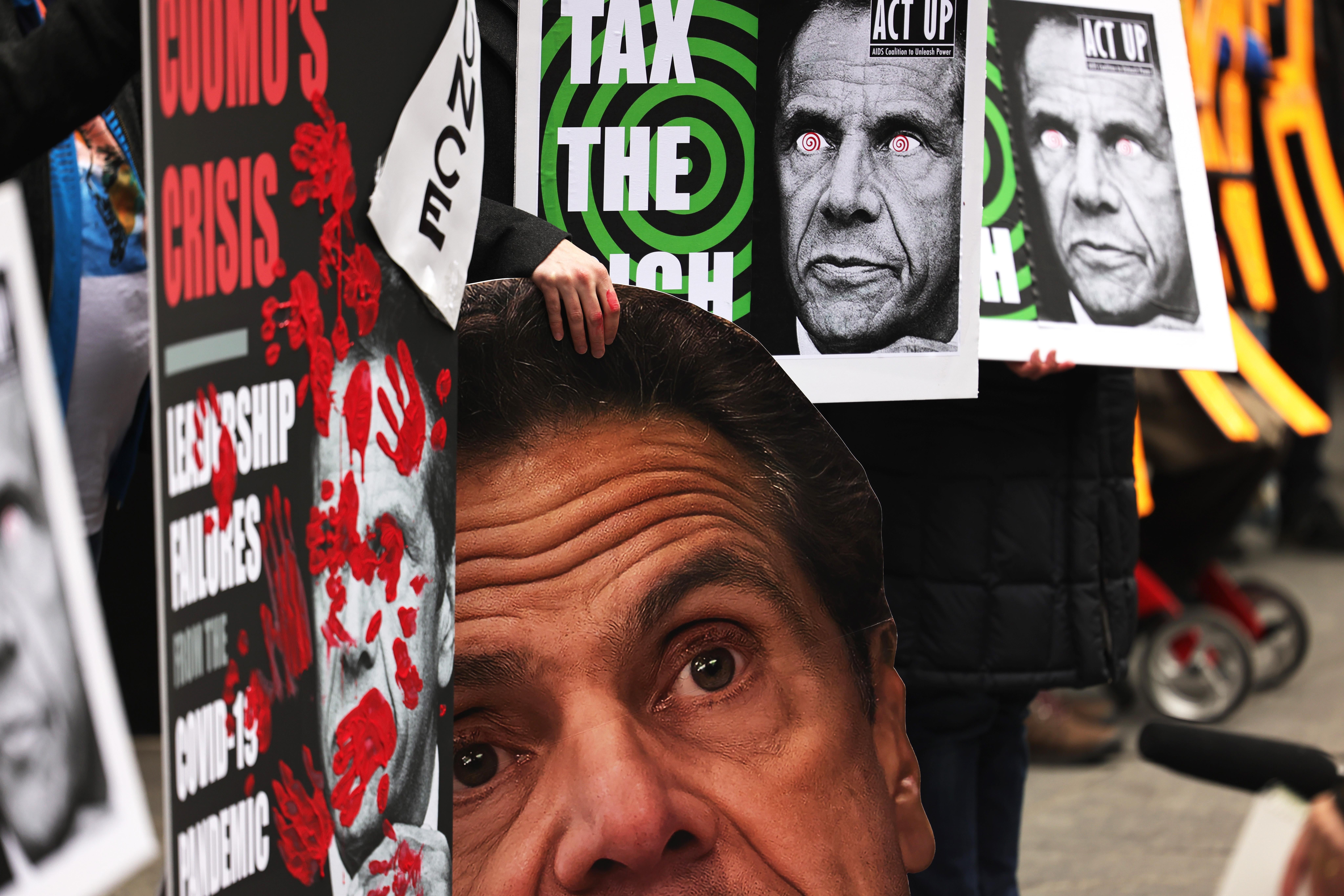 A row of protesters holding signs with Cuomo's picture on them that say "Cuomo's Crisis" and "Tax the Rich"