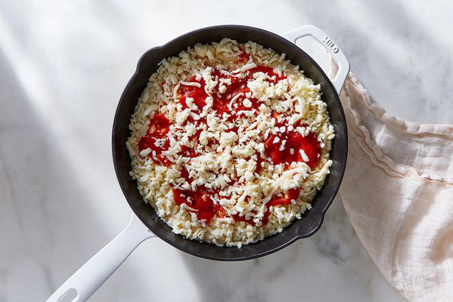 Tomato sauce and unmelted shredded cheese on top of dough in a pan.