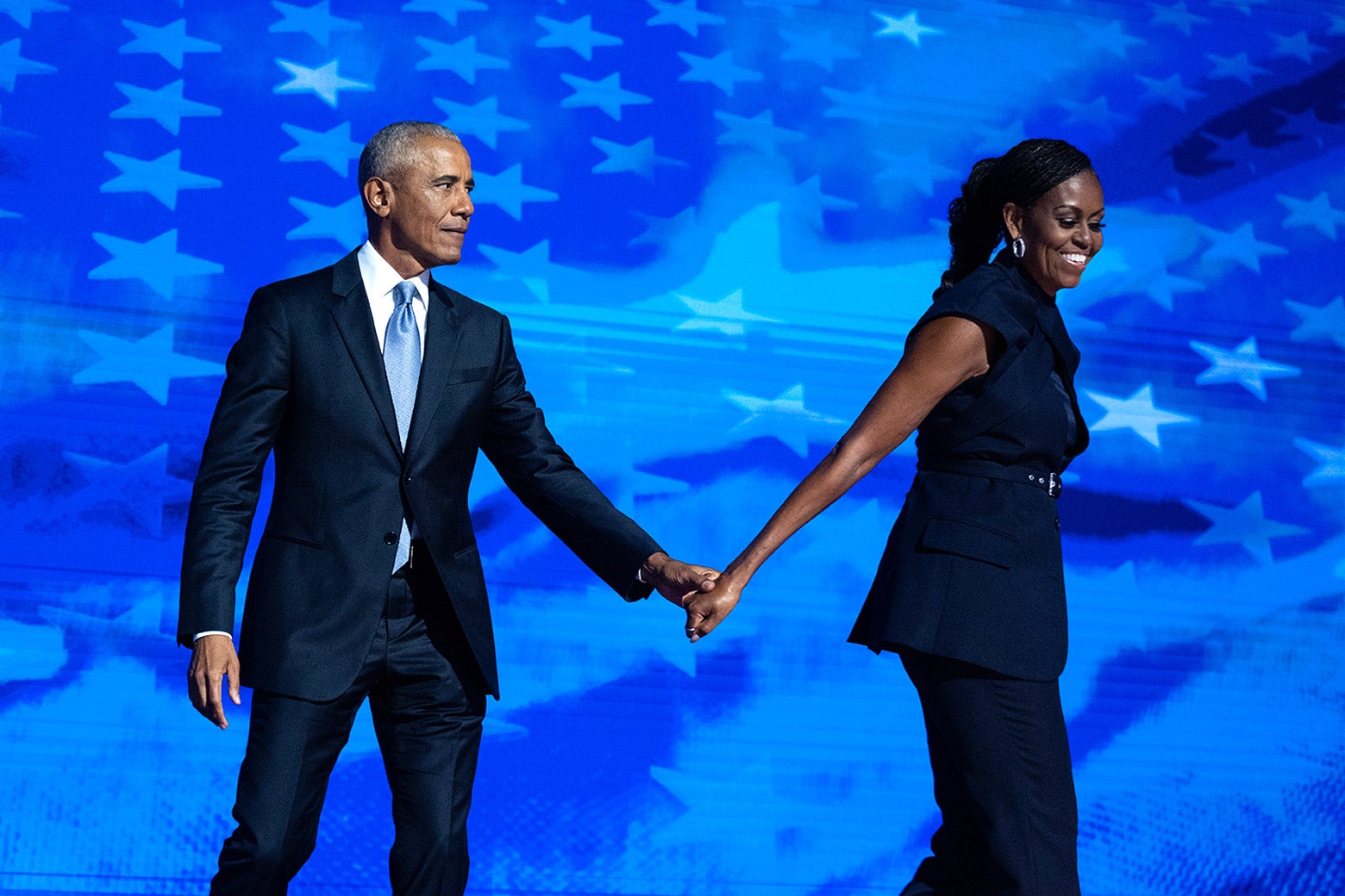 Barack Obama holding the hand of Michelle Obama as she walks away.