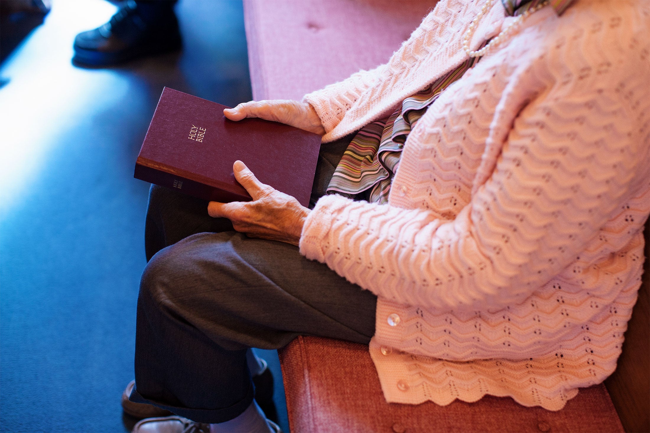 An elderly woman sits in a pew, holding a Bible.