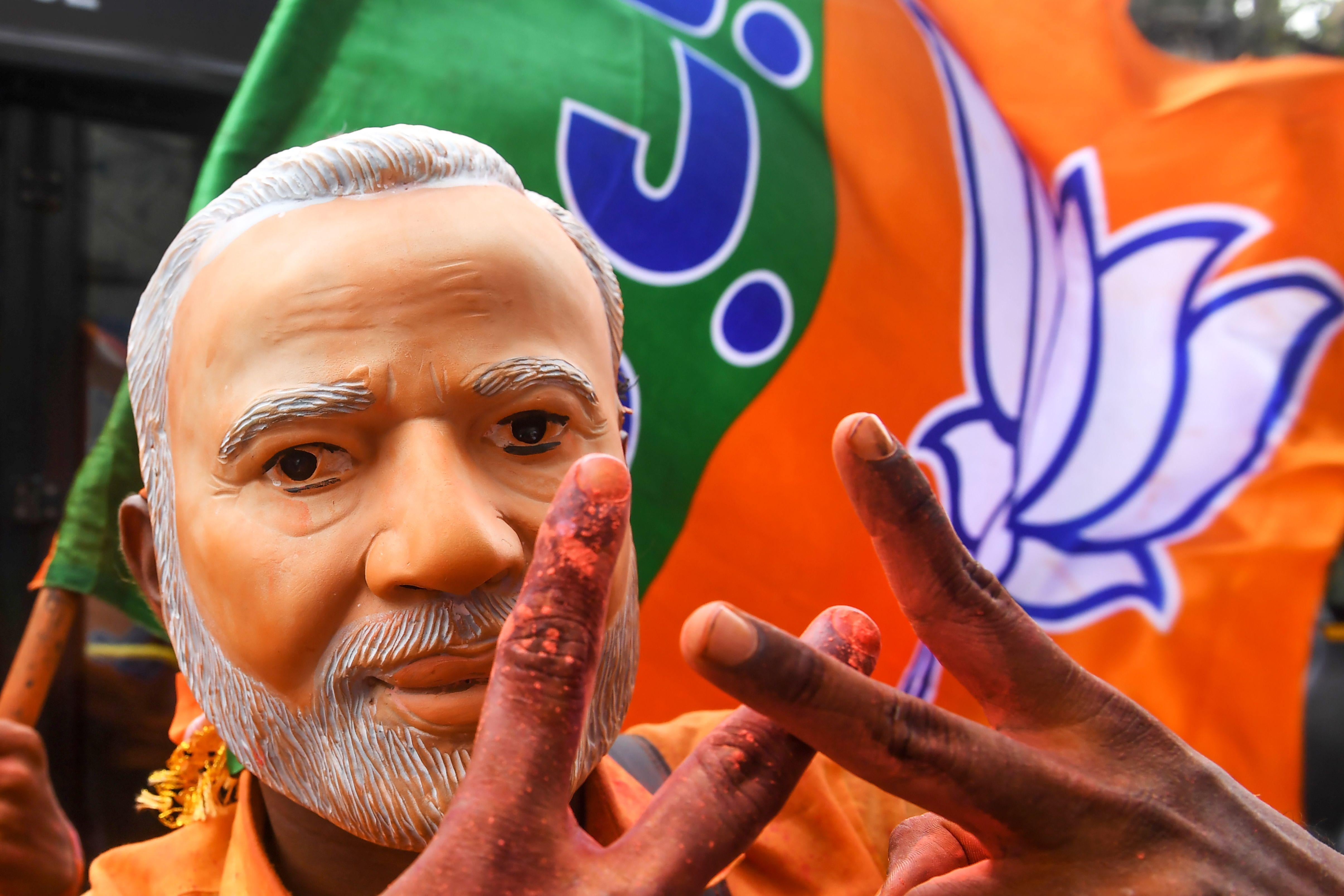An Indian supporter of Bharatiya Janata Party (BJP) wearing a mask of Prime Minister Narendra Modi flahes the victory sign as he celebrates on the vote results day for India's general election in Kolkata on May 23, 2019.
