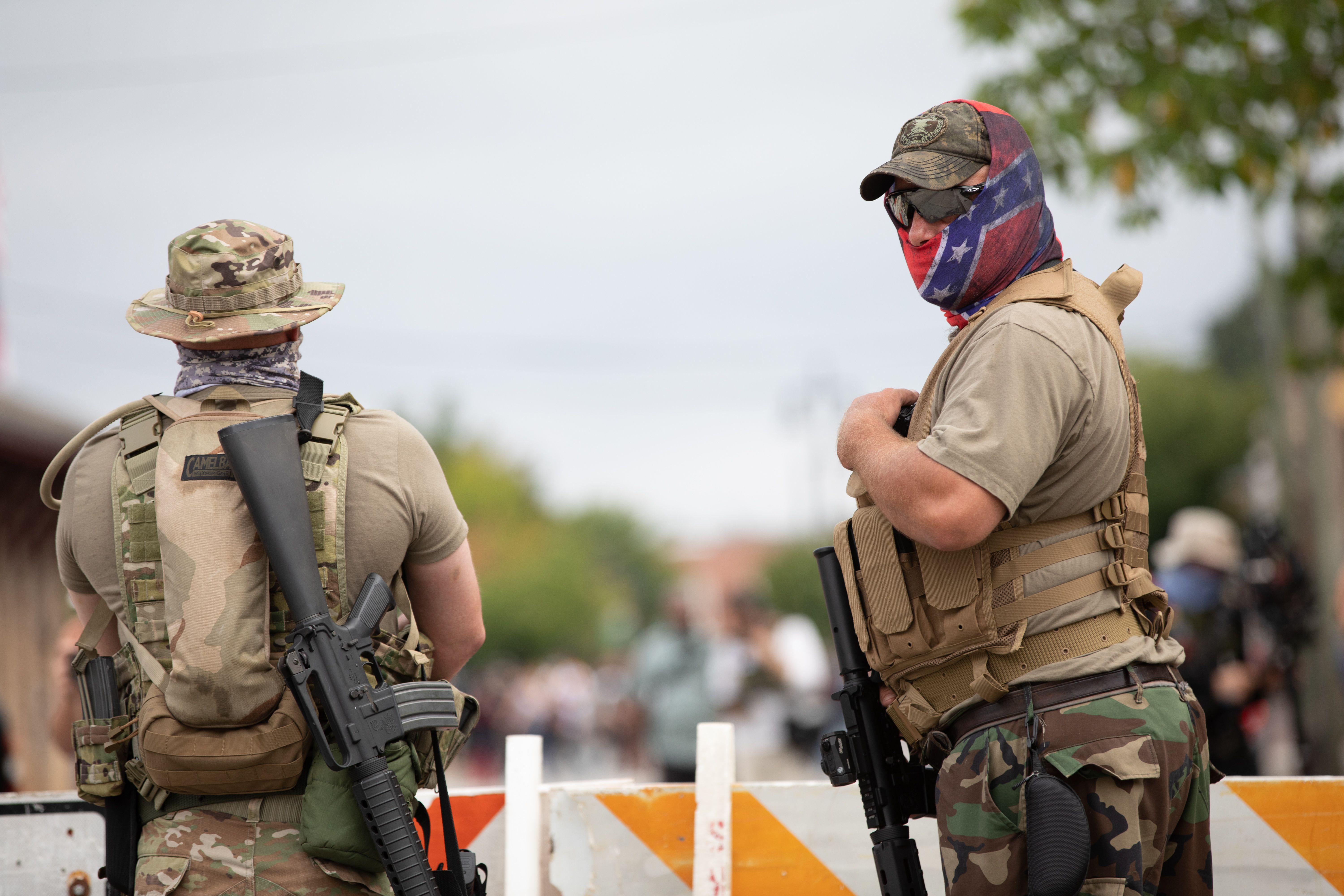 Two armed militia members, one wearing a confederate flag mask. 