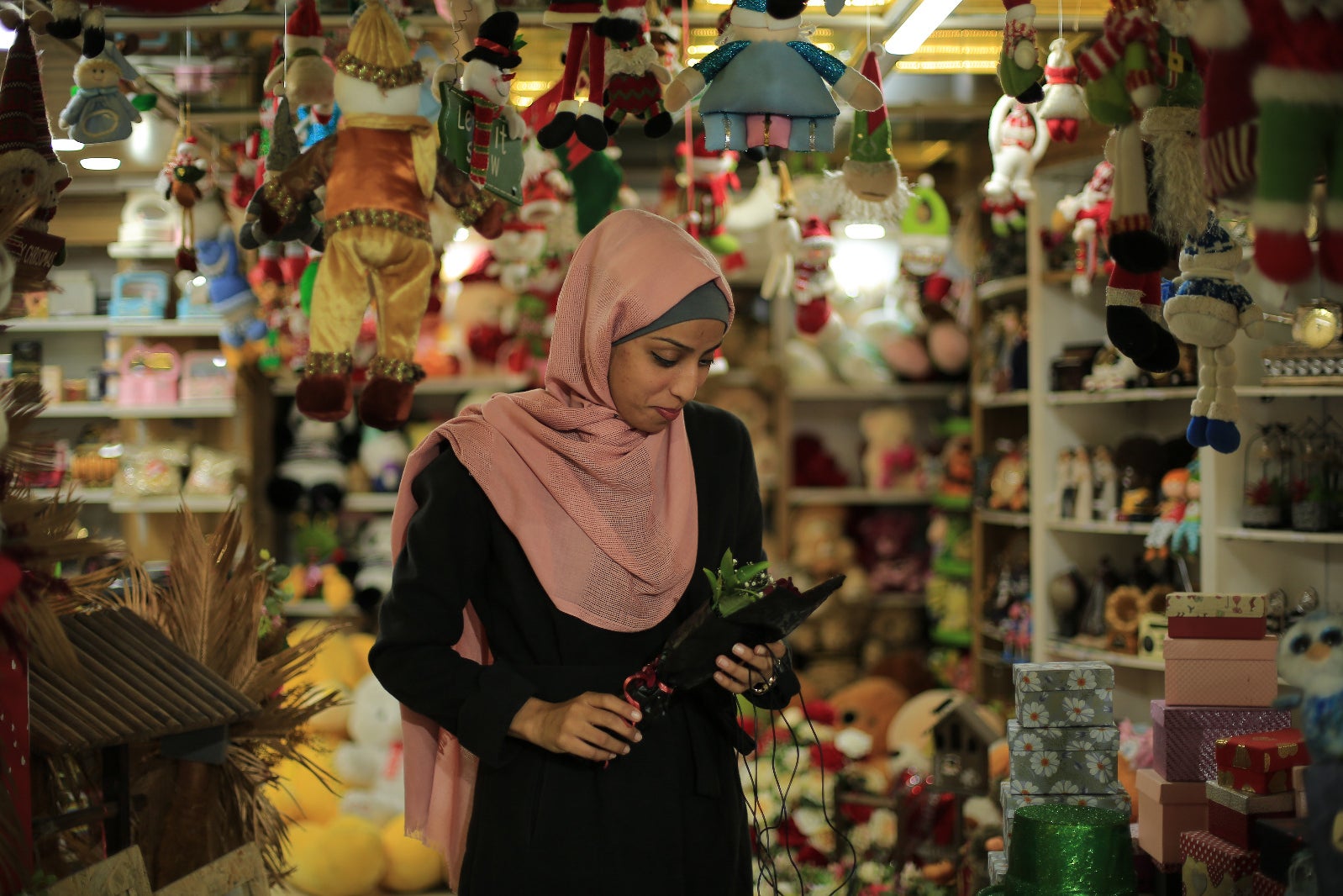 A woman in hijab looks at a leafy decoration as ornaments and toys hang around the shop around her