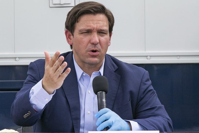 Ron DeSantis speaks and holds a mic with a gloved hand.