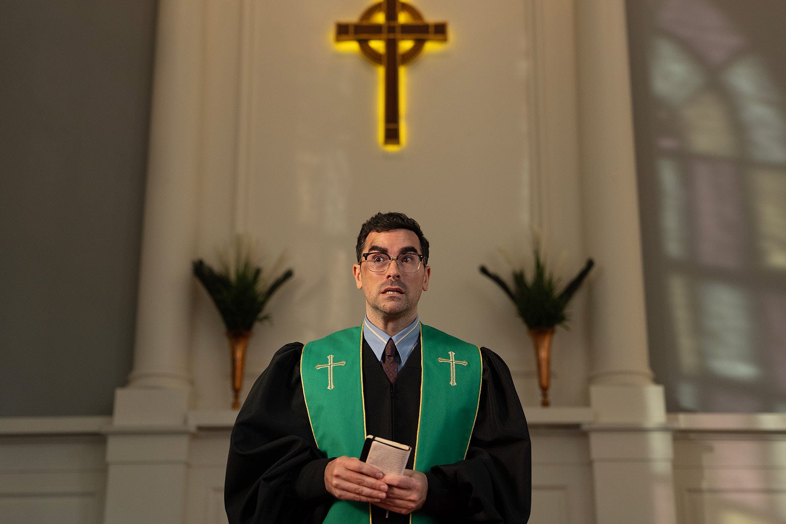 Dan Levy as Nicky, dressed as a pastor in a church.