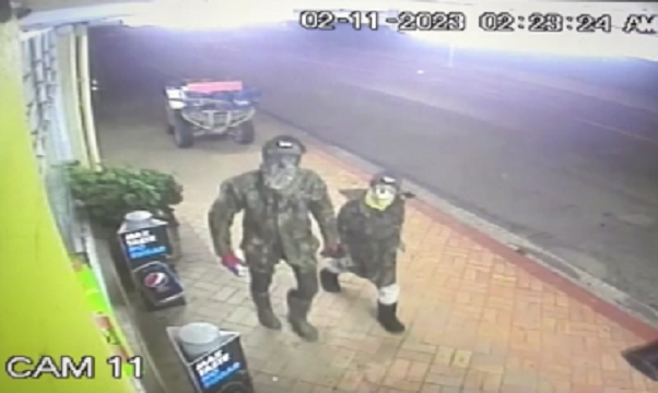 Surveillance camera footage of two figures, one an adult and the other a child, in face masks and camo gear walking down a sidewalk.