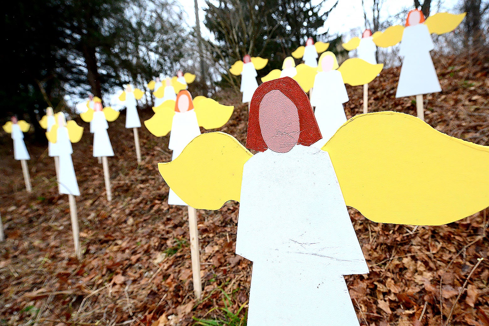 Wood cutouts of angels are seen posted on a small hill covered with fallen leaves.