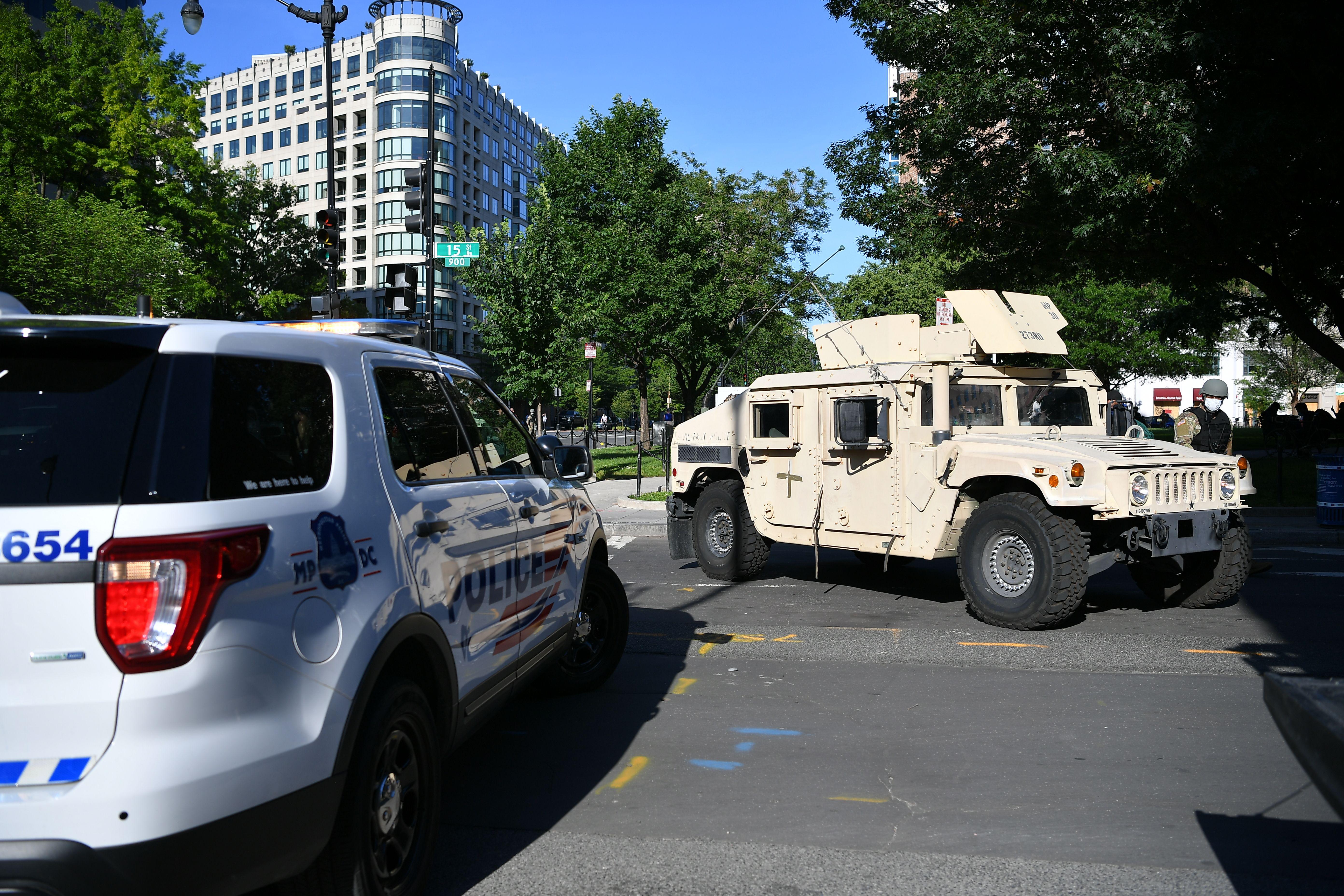 A tank and a police van block a road.
