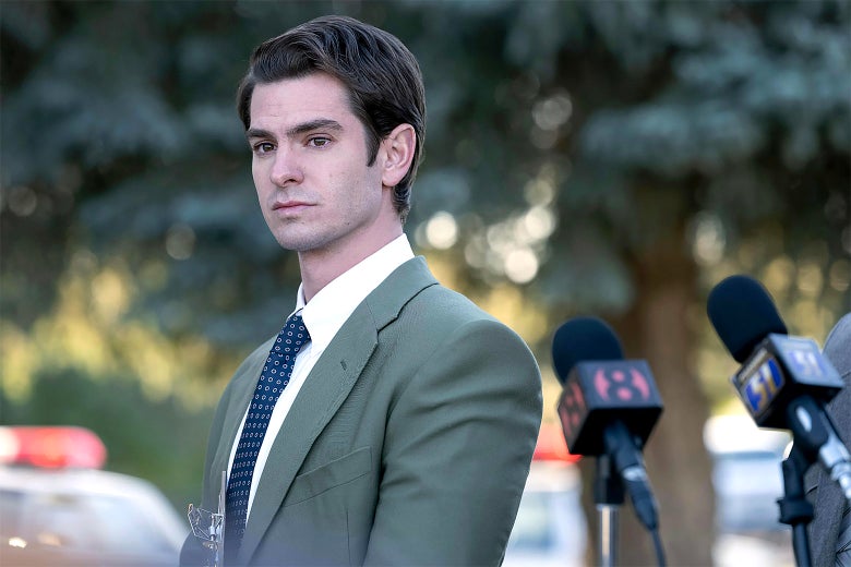Andrew Garfield in Under the Banner of Heaven standing near a podium in a green suit and blue tie.