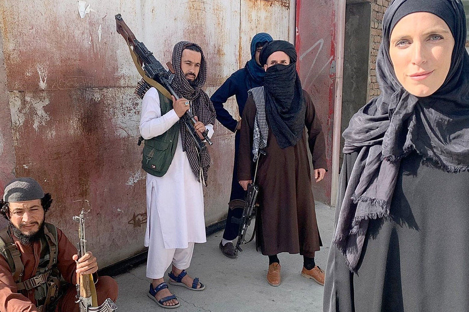 Ward wearing a black abaya and headscarf, Clarissa Ward stands beside four Taliban fighters with guns outside.