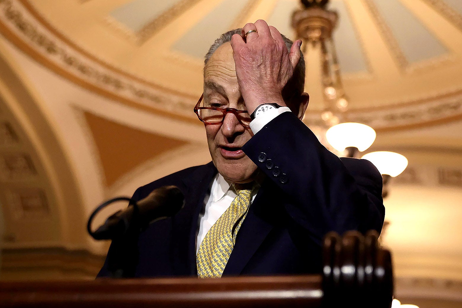 Chuck Schumer holds his hand to his head.
