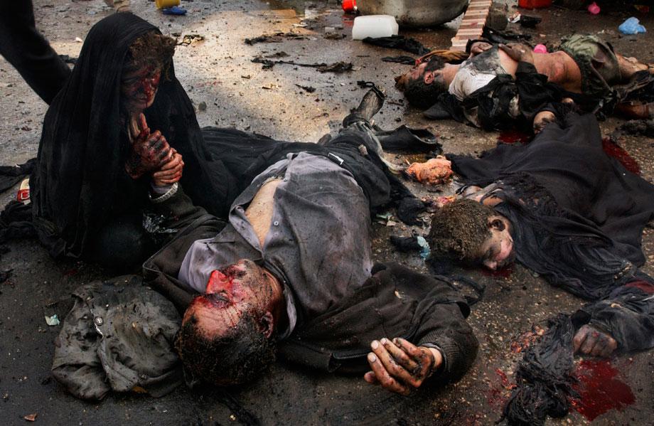 KARBALA, Iraq—An Iraqi woman holds the hand of her dying husband as he lies among the bodies of their children, who were also killed by a suicide bombing during the Shi'ite festival of Ashura. The mother is the only family member to survive, March 2, 2004.