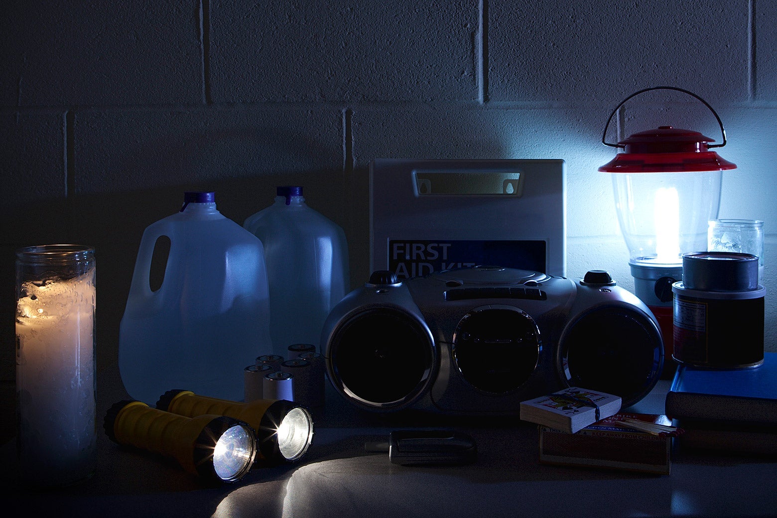 A table containing jugs of water, a radio, playing cards, a candle, two flashlights and a lantern during a blackout.